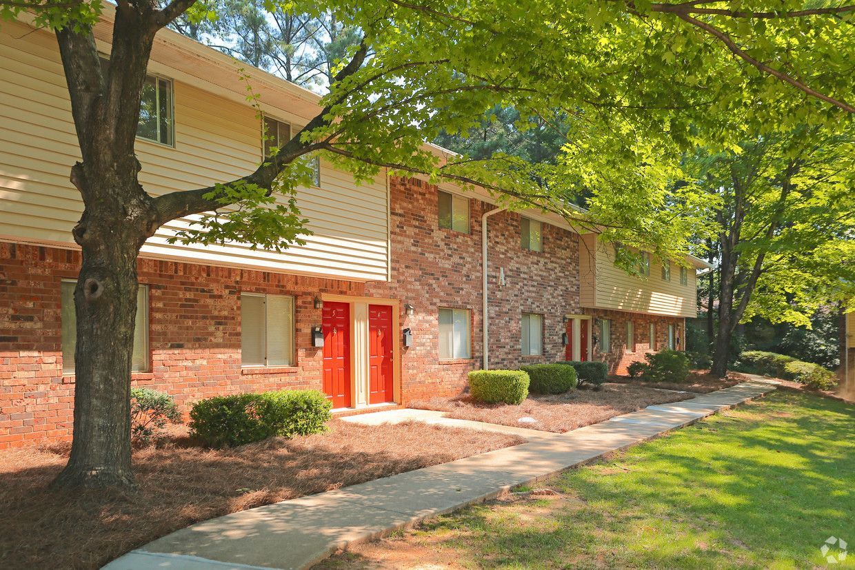 Brick apartment building with red doors, trees, and a shaded sidewalk along the front
