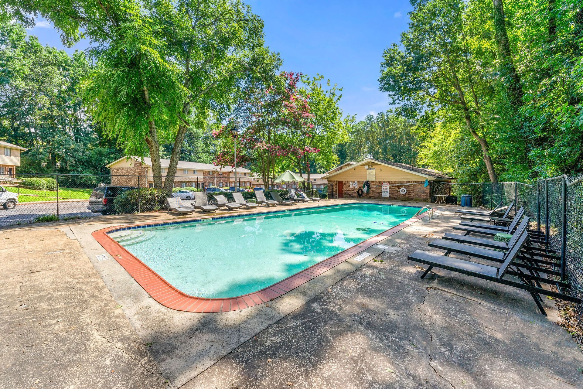 Outdoor swimming pool surrounded by lounge chairs and trees on a sunny day