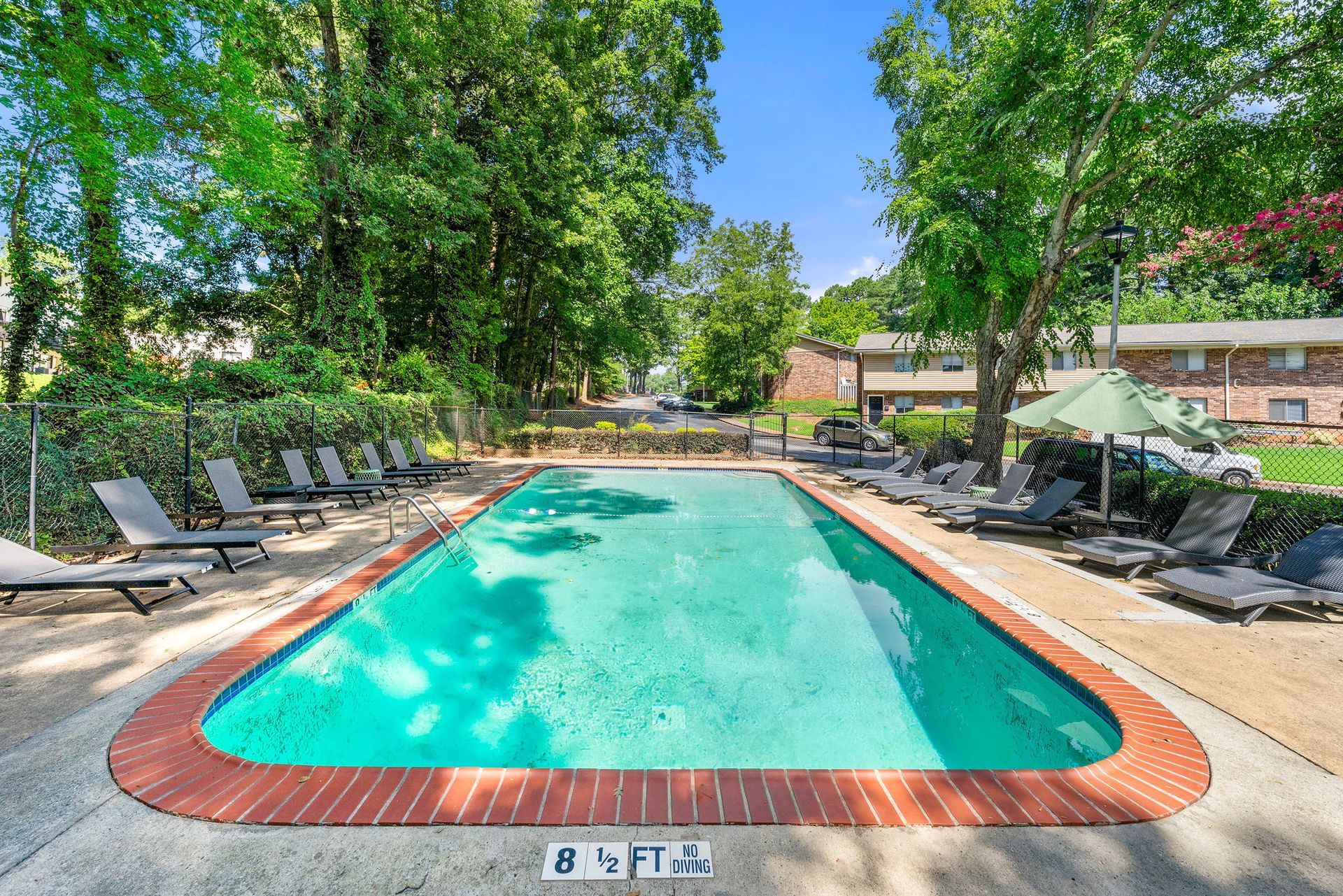 Outdoor swimming pool surrounded by lounge chairs and trees under a bright blue sky