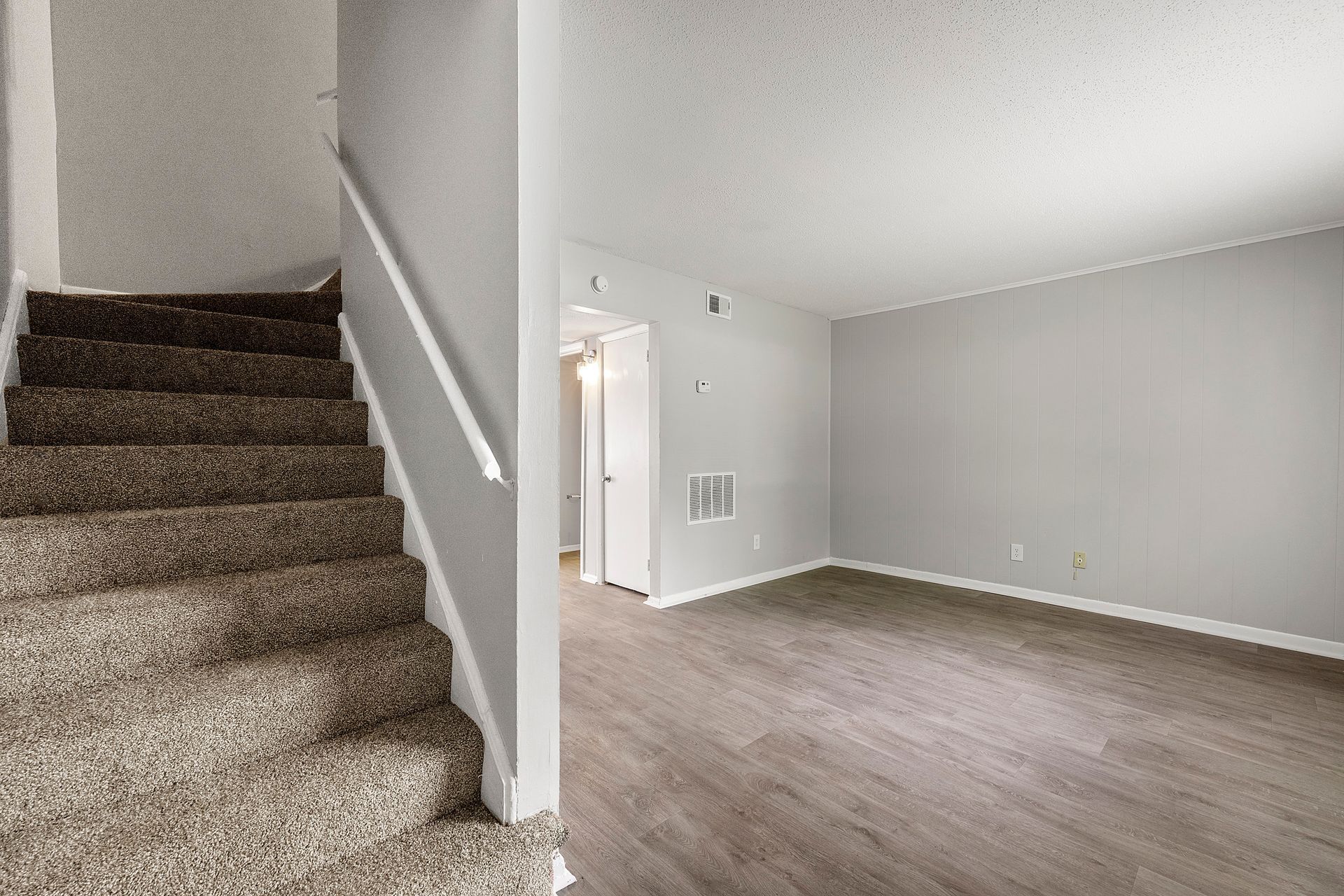 Carpeted stairs beside an open living room with gray walls and wood-look flooring