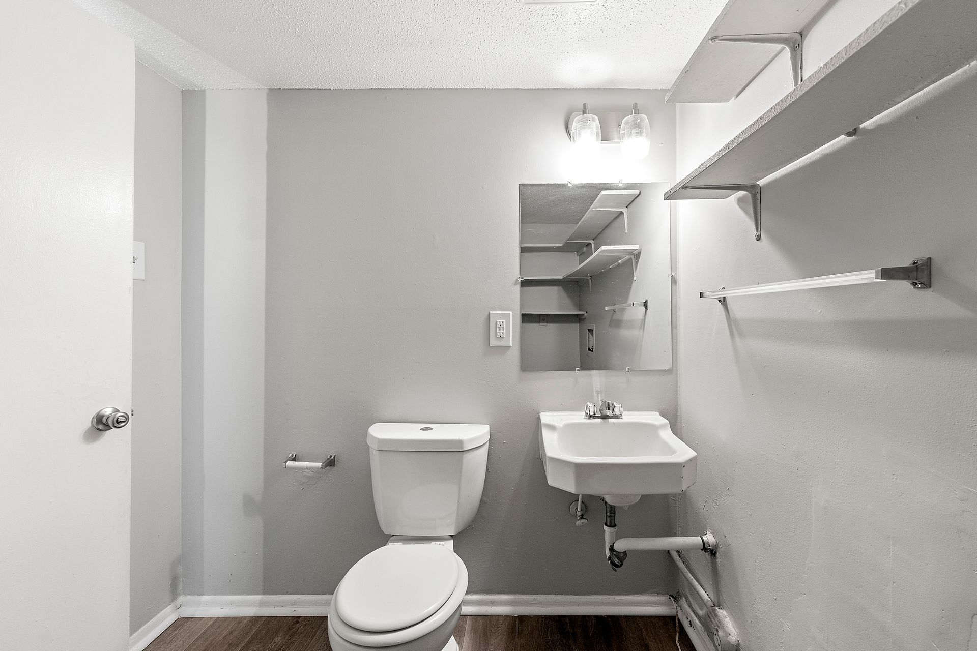 Small bathroom with toilet, wall-mounted sink, mirror, towel bars, and gray walls.