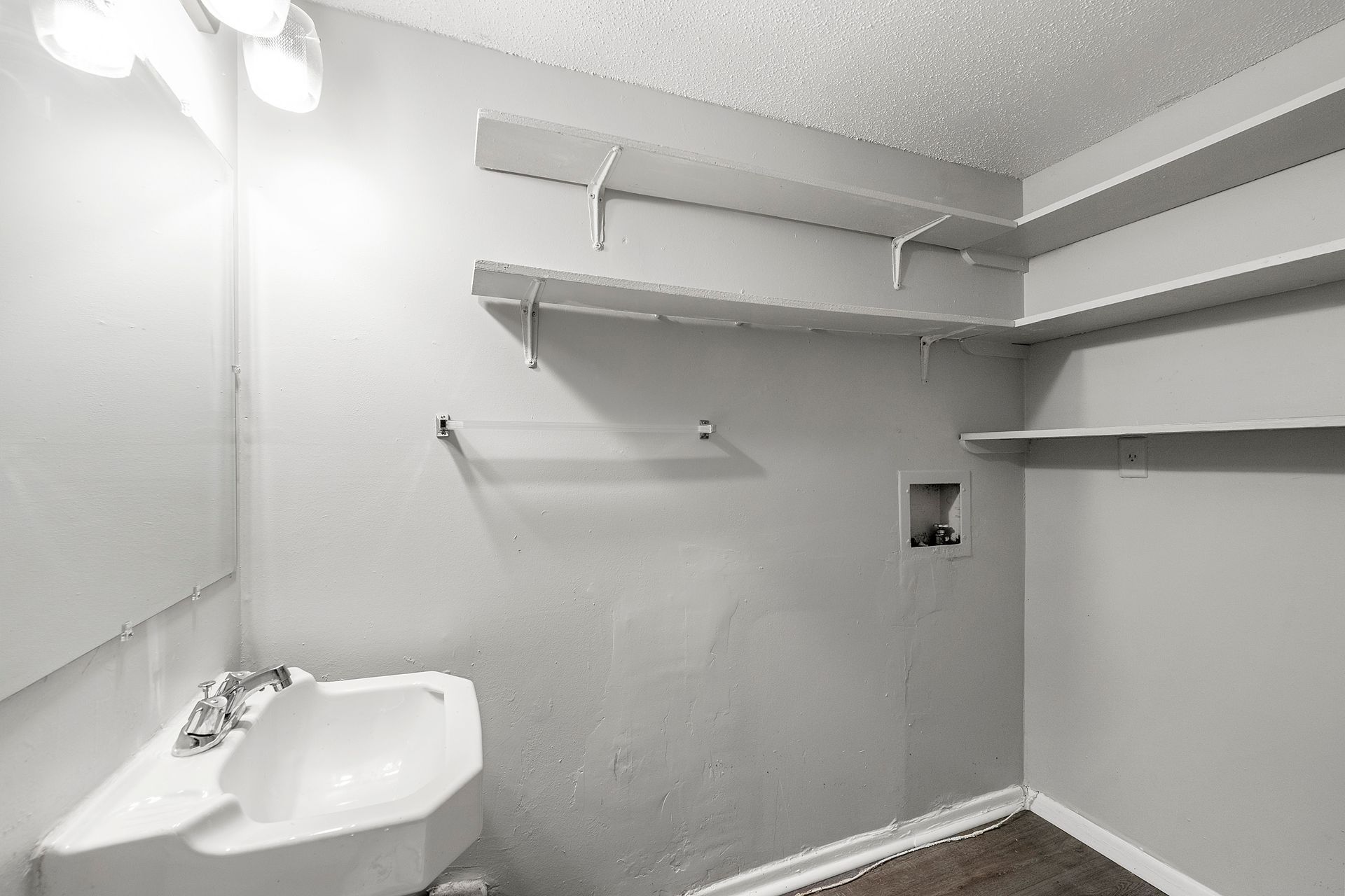 Small white laundry room with sink, shelves, and wall-mounted utility opening