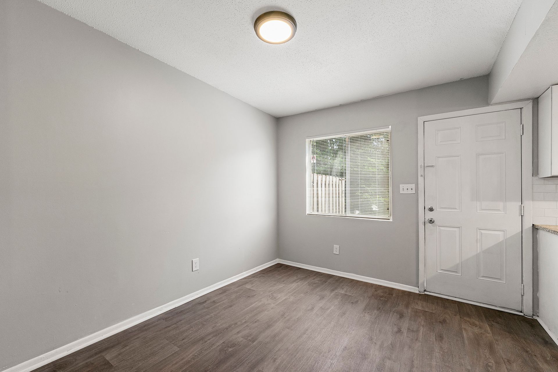 Empty white bedroom with gray carpet, window blinds, and a ceiling light