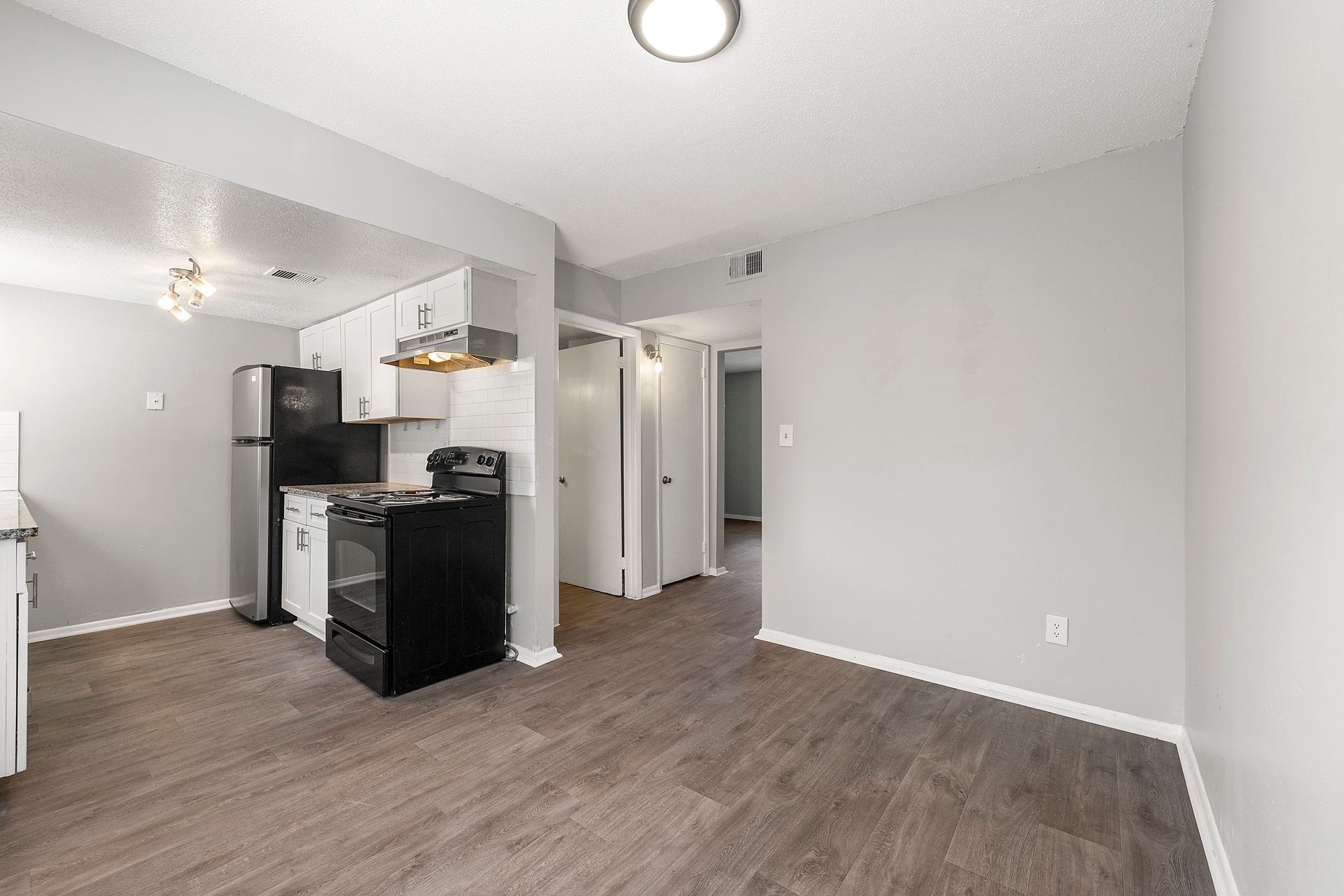 Empty apartment living area with kitchen, gray walls, and dark wood flooring
