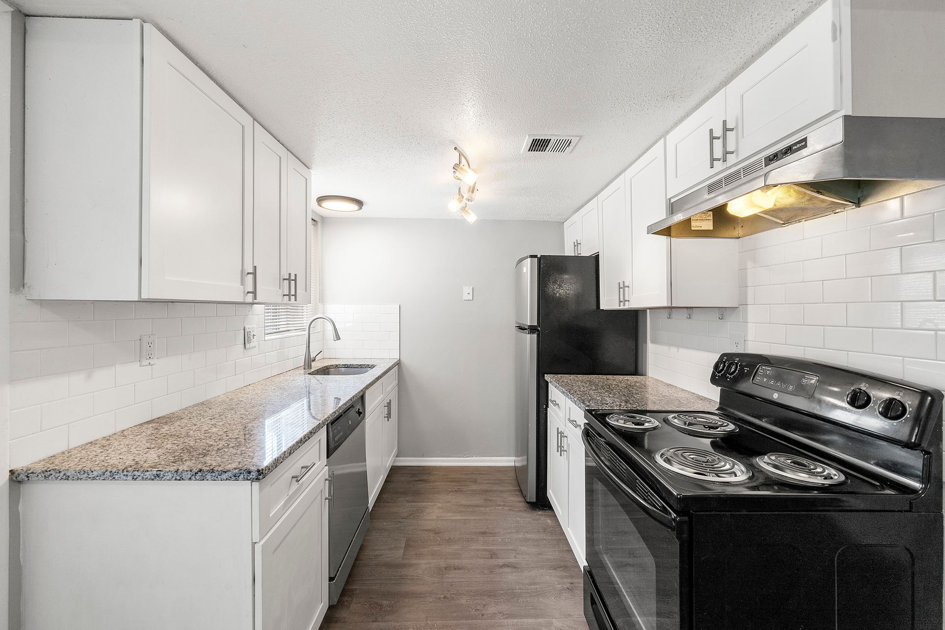 Bright galley kitchen with white cabinets, black stove, and granite countertops