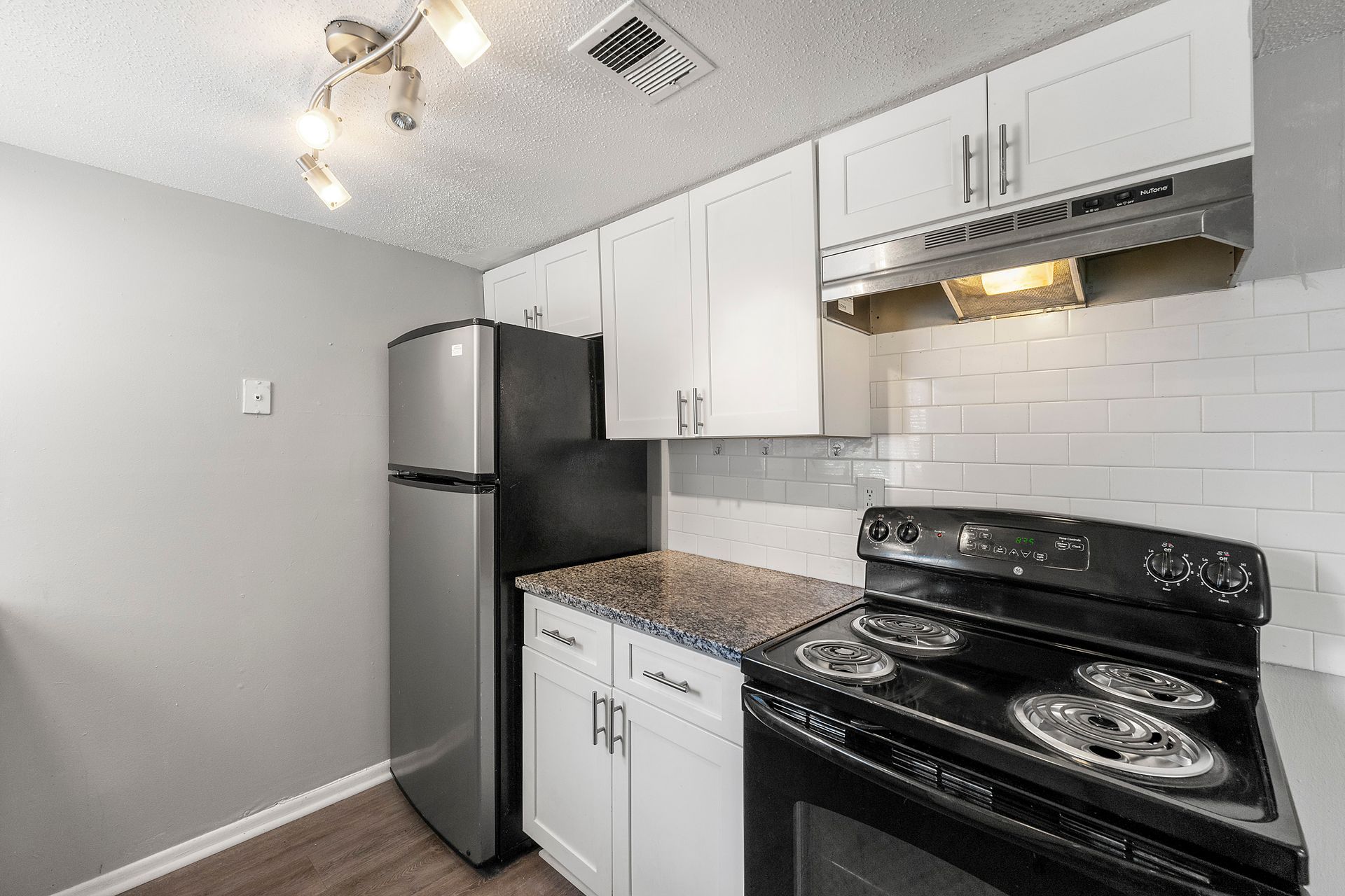 Small modern kitchen with white cabinets, black stove, stainless fridge, and gray walls.