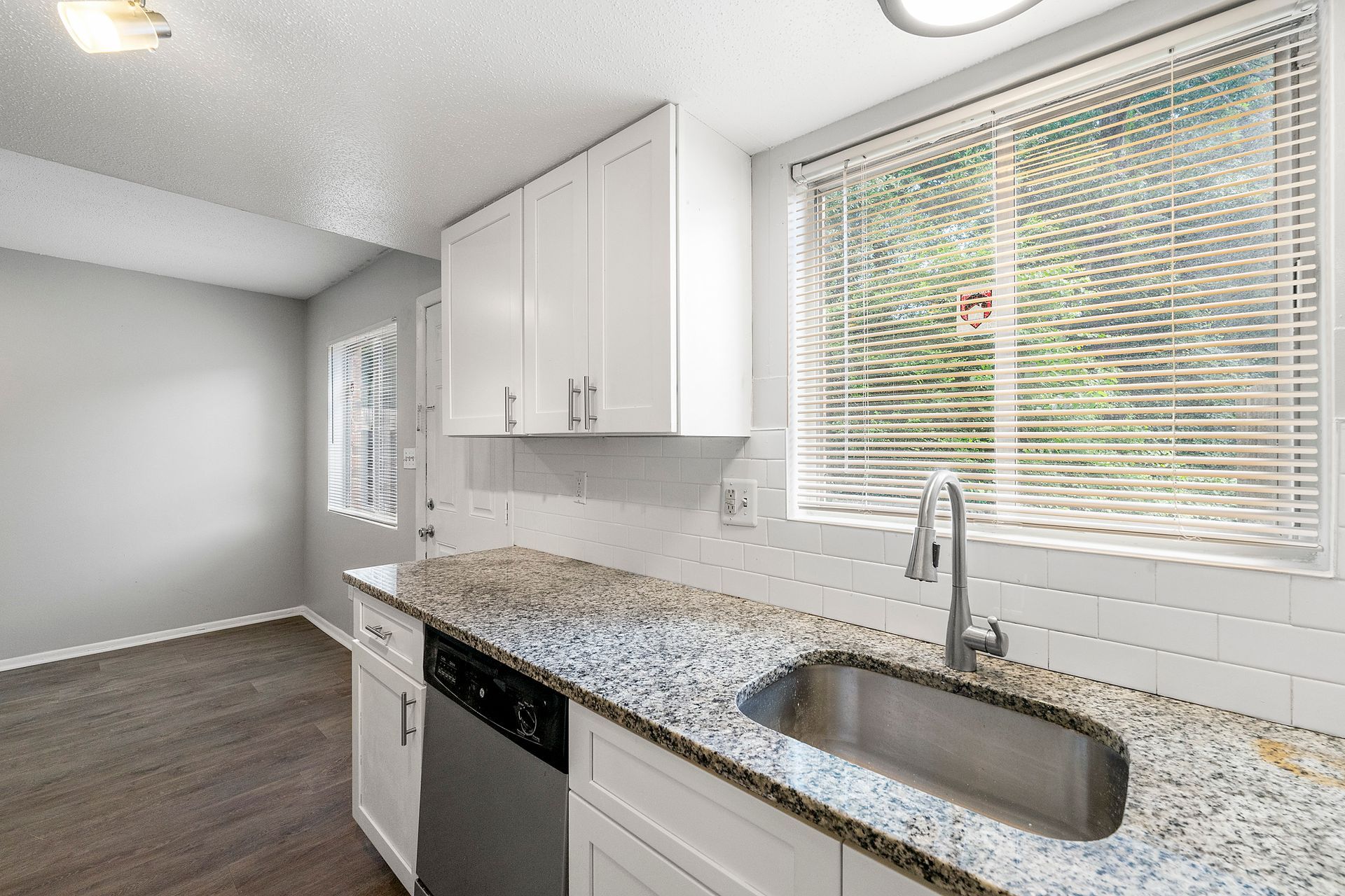 Bright modern kitchen with white cabinets, granite countertop, sink, dishwasher, and large window blinds