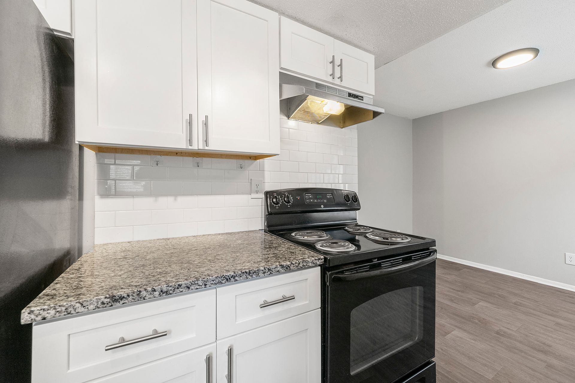Small kitchen with white cabinets, granite countertop, black stove, and gray walls in a bright apartment.