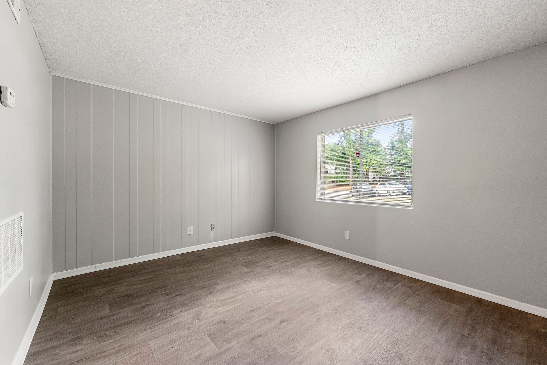 Empty gray bedroom with beige carpet and a window overlooking trees