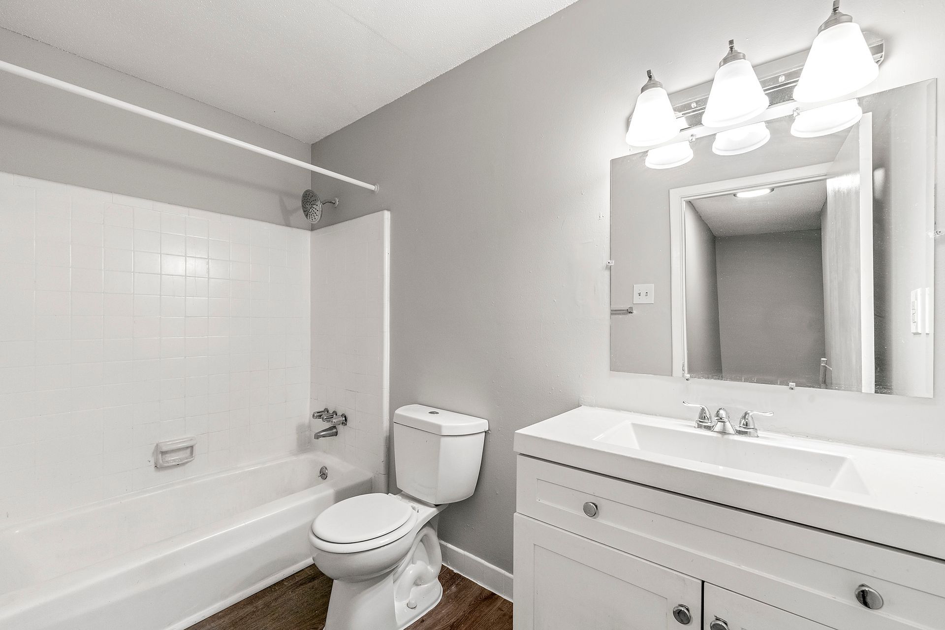 White bathroom with tub, toilet, vanity, and large mirror under bright lights