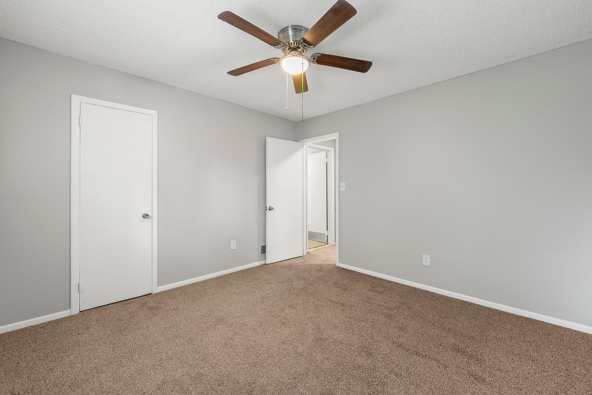 Empty gray bedroom with carpet, white doors, and a ceiling fan.