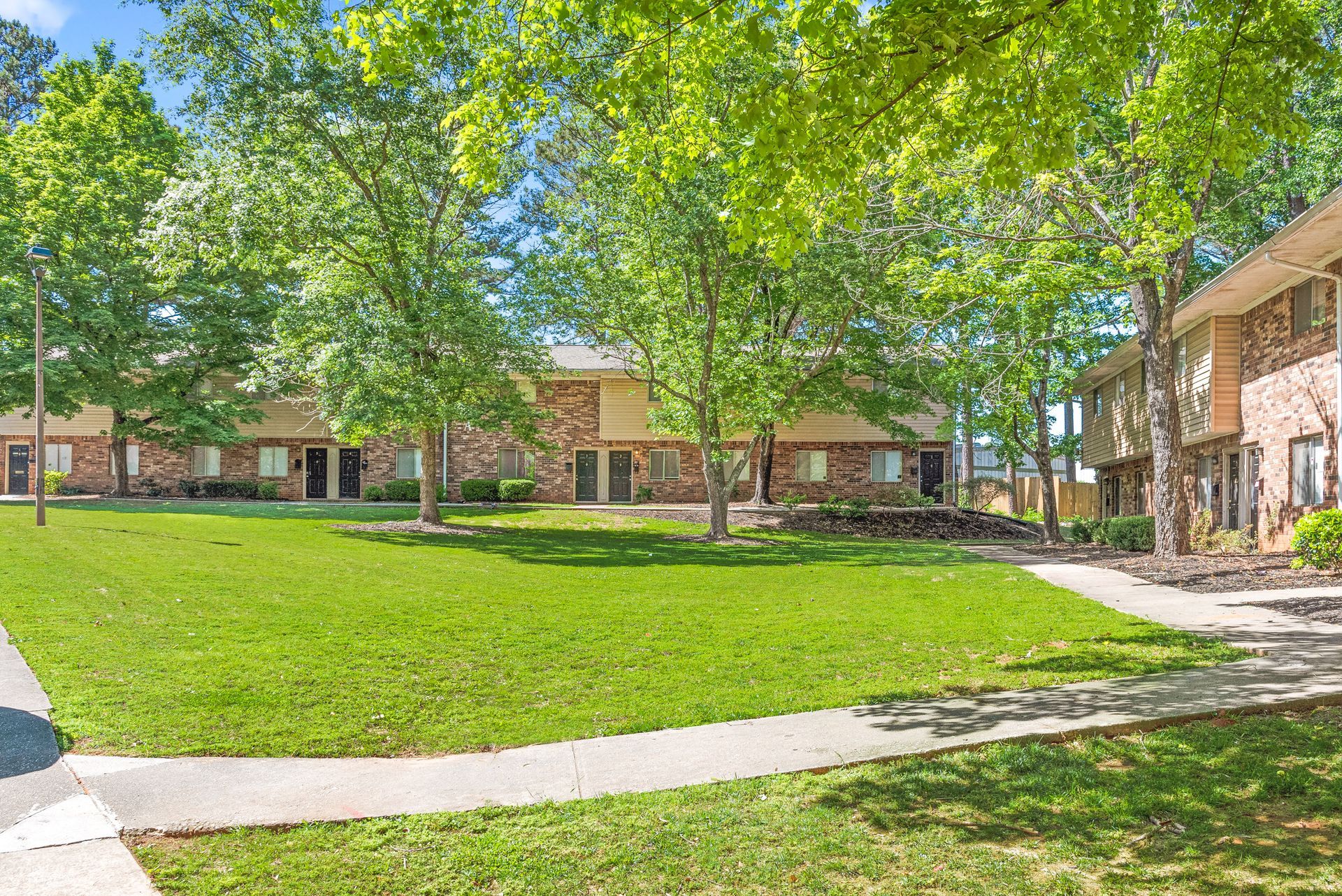 Sunny courtyard with green lawn, trees, and brick apartment buildings surrounding a walkway