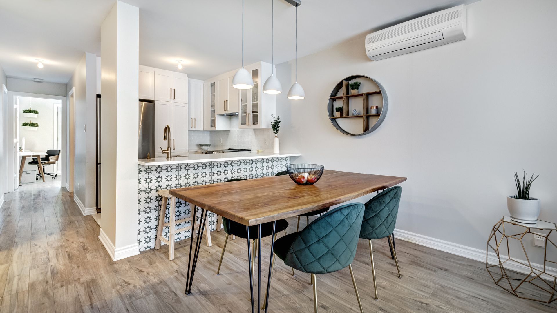 Bright modern dining area beside white kitchen, with wooden table, teal chairs, pendant lights, and wall decor