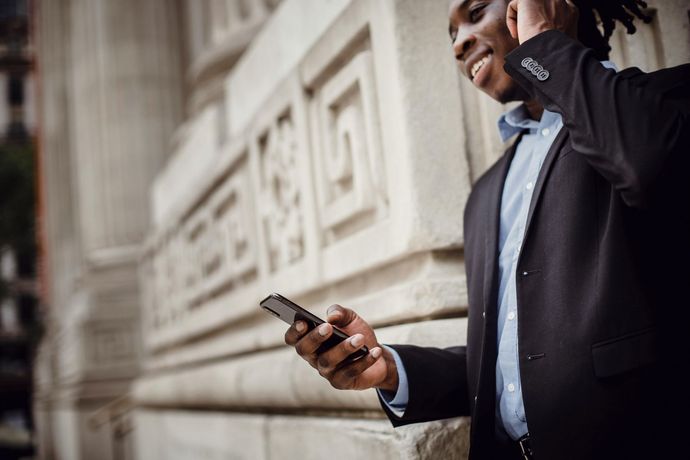 A man in a suit is talking on a cell phone while standing next to a building.