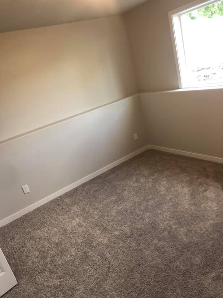 An empty room with beige upper walls, grey lower walls, and grey carpet, featuring a large window.