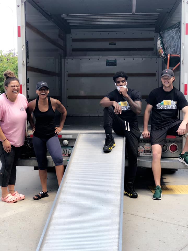 Four people smile while standing near an open moving truck with a metal ramp extended to the ground.