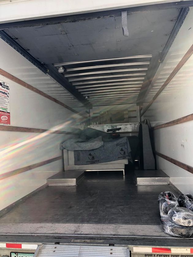The interior of a moving truck with furniture covered in protective blankets and some items placed on the floor.