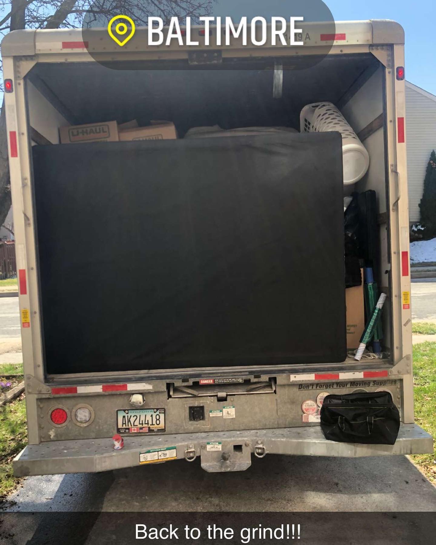 The open rear of a moving truck parked in Baltimore, filled with a large black furniture cover and various moving boxes.