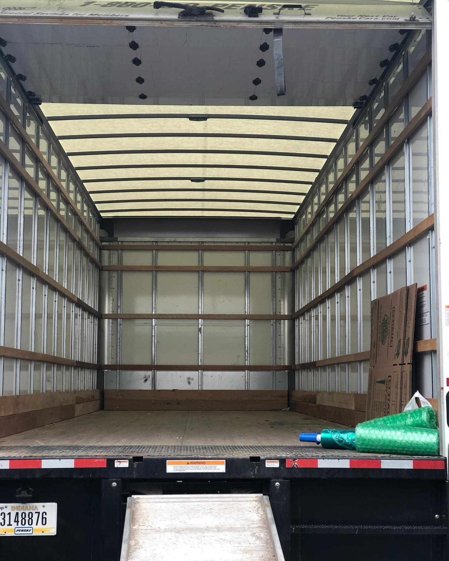 The interior of an empty box truck with a metal floor, wooden wall slats, a translucent roof, and a loading ramp.