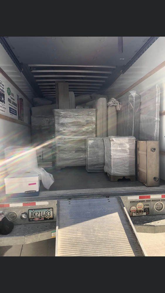 The interior of a moving truck packed with furniture and boxes wrapped in protective plastic.