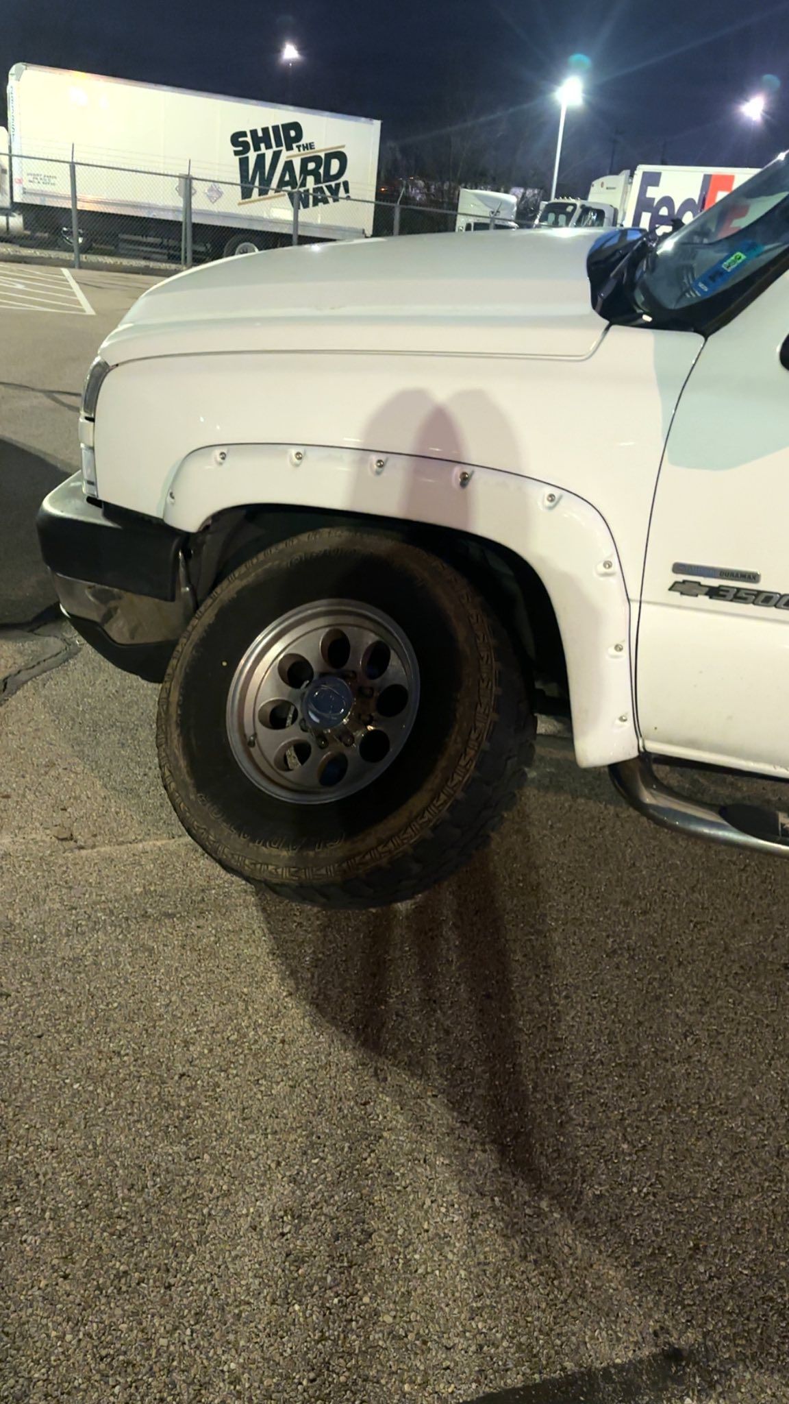 White pickup truck with a dirty tire, parked in a parking lot at night.