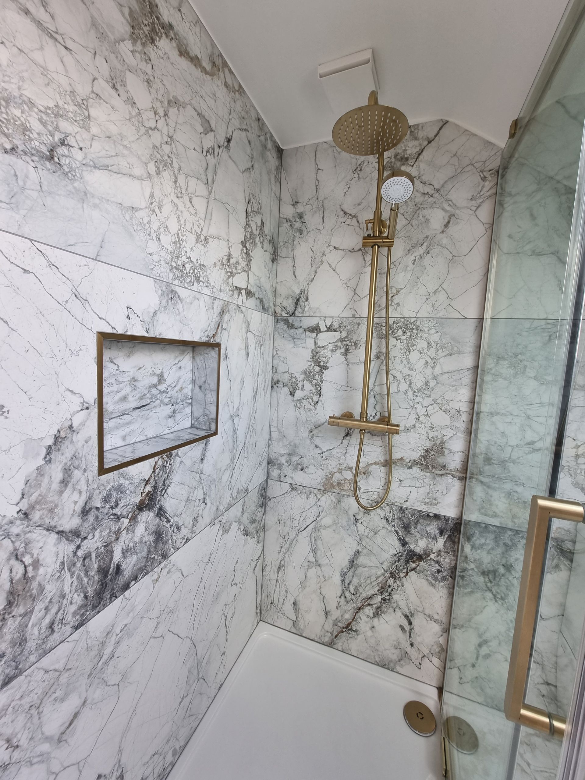 A bathroom with marble tiles and a shower with a gold shower head.