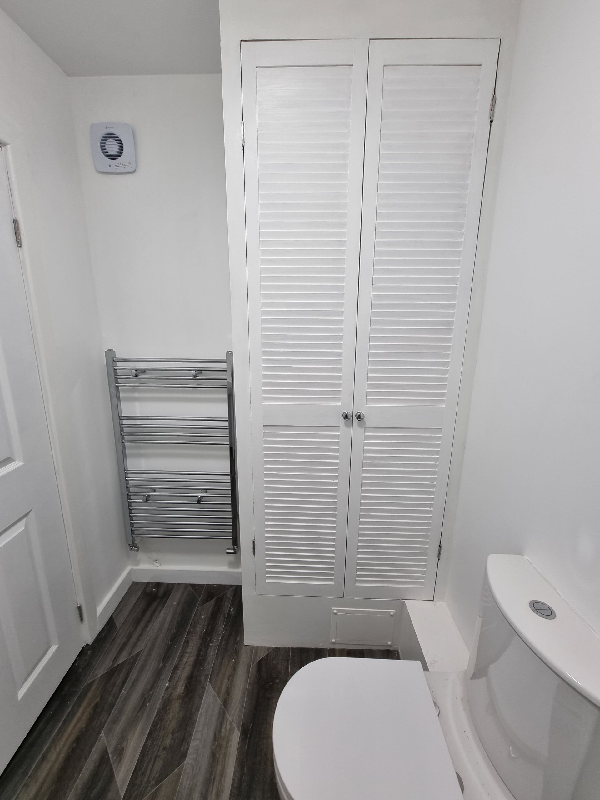 White bathroom with gray flooring, towel warmer, toilet, and shuttered closet.