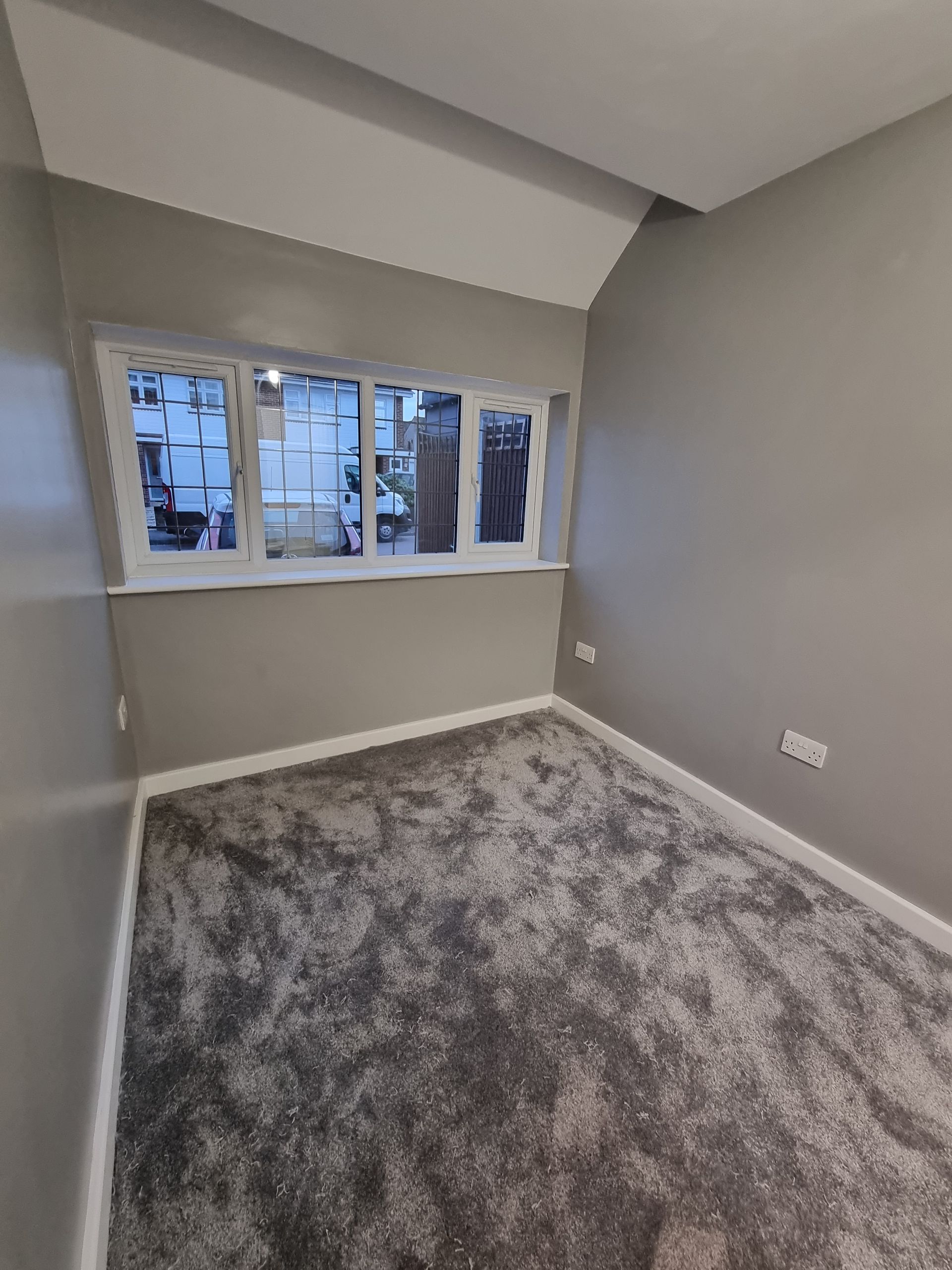 Small, empty room with gray walls, white trim, and a window. Gray, textured carpet.