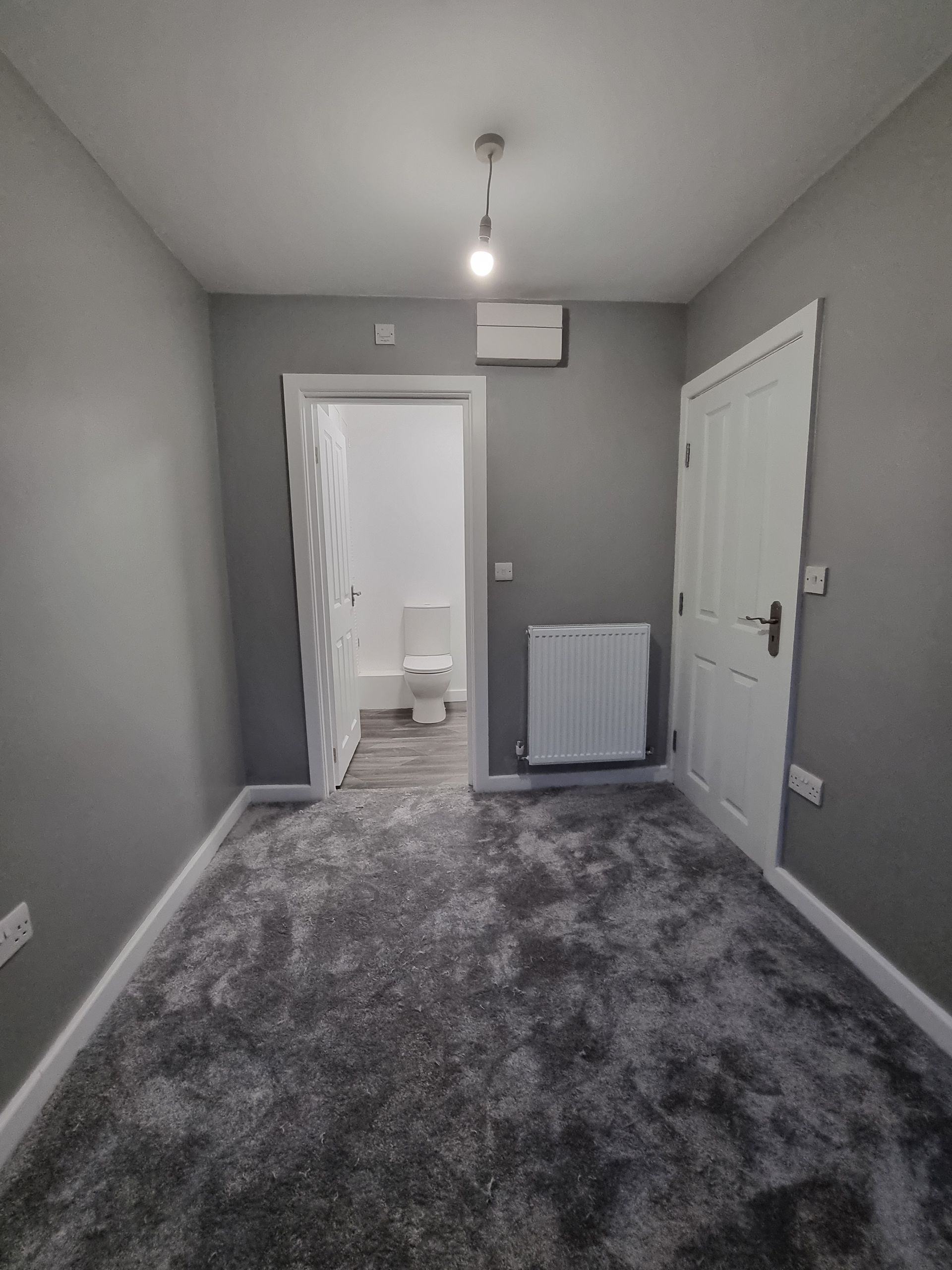 Empty room with gray walls, fluffy gray carpet, white doors, and a doorway to a bathroom.