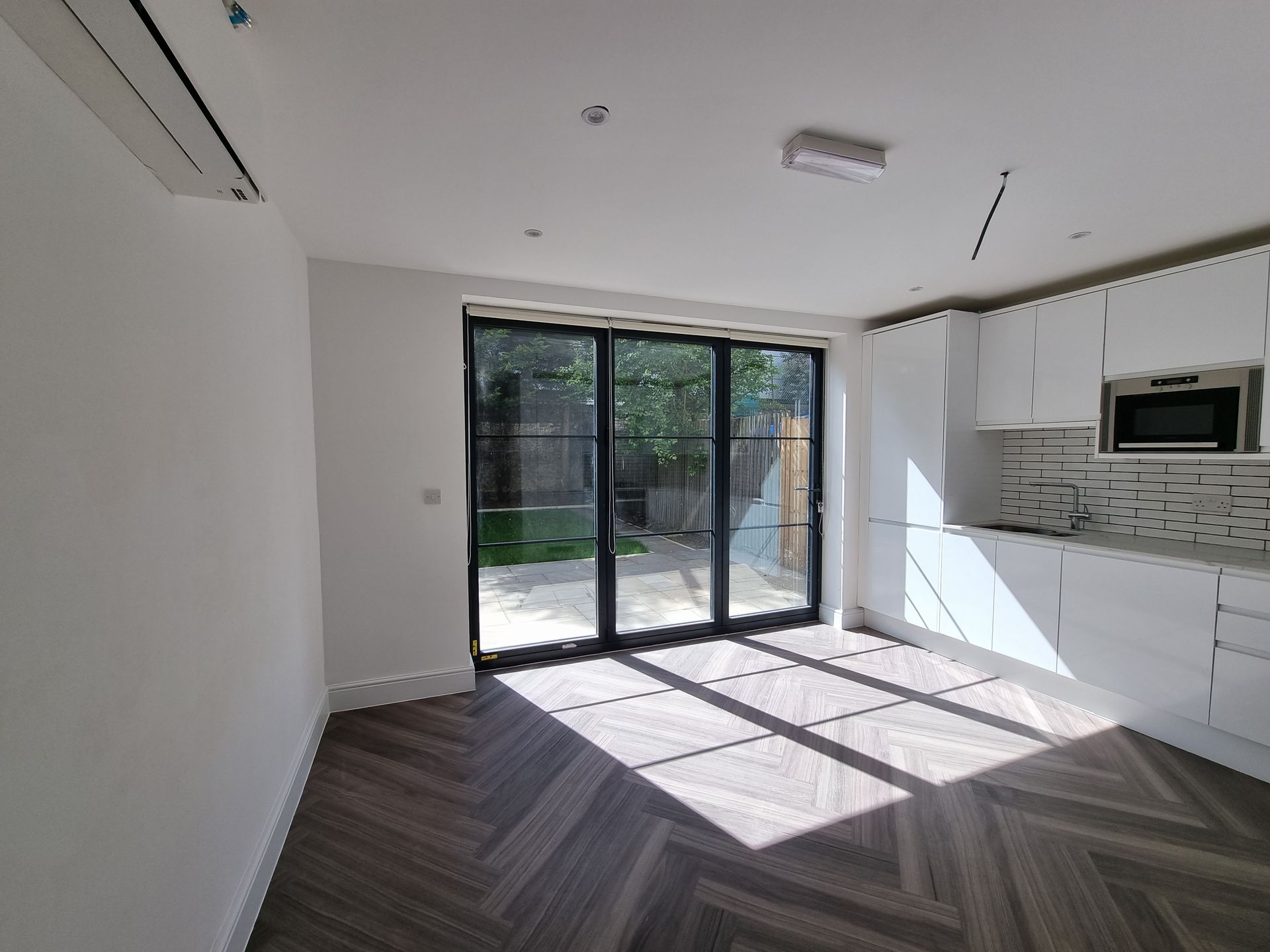 Interior of a kitchen with white cabinets, dark-framed glass doors, and herringbone patterned flooring.