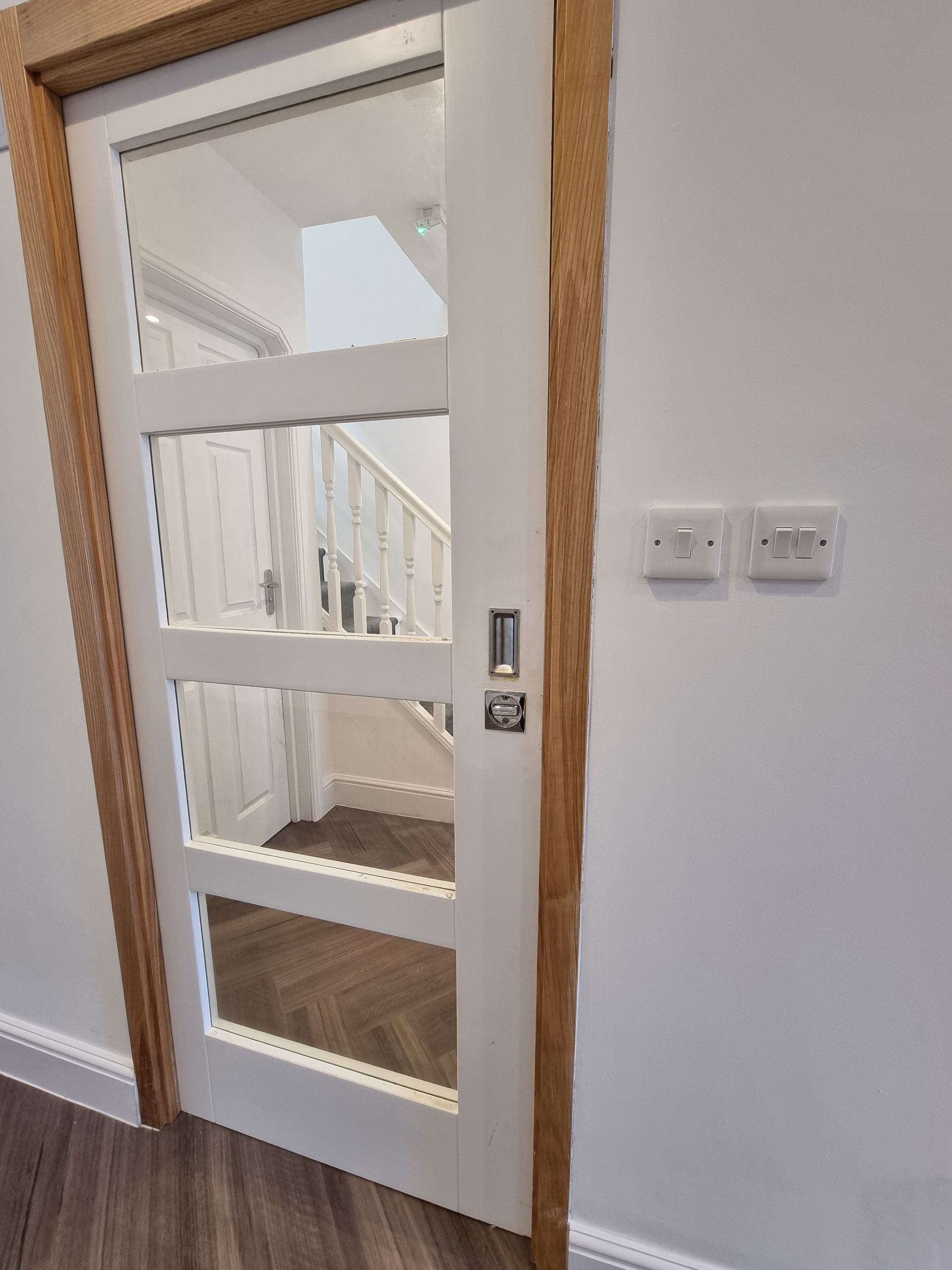 Pocket door with glass panels and wooden frame, revealing a hallway with stairs.