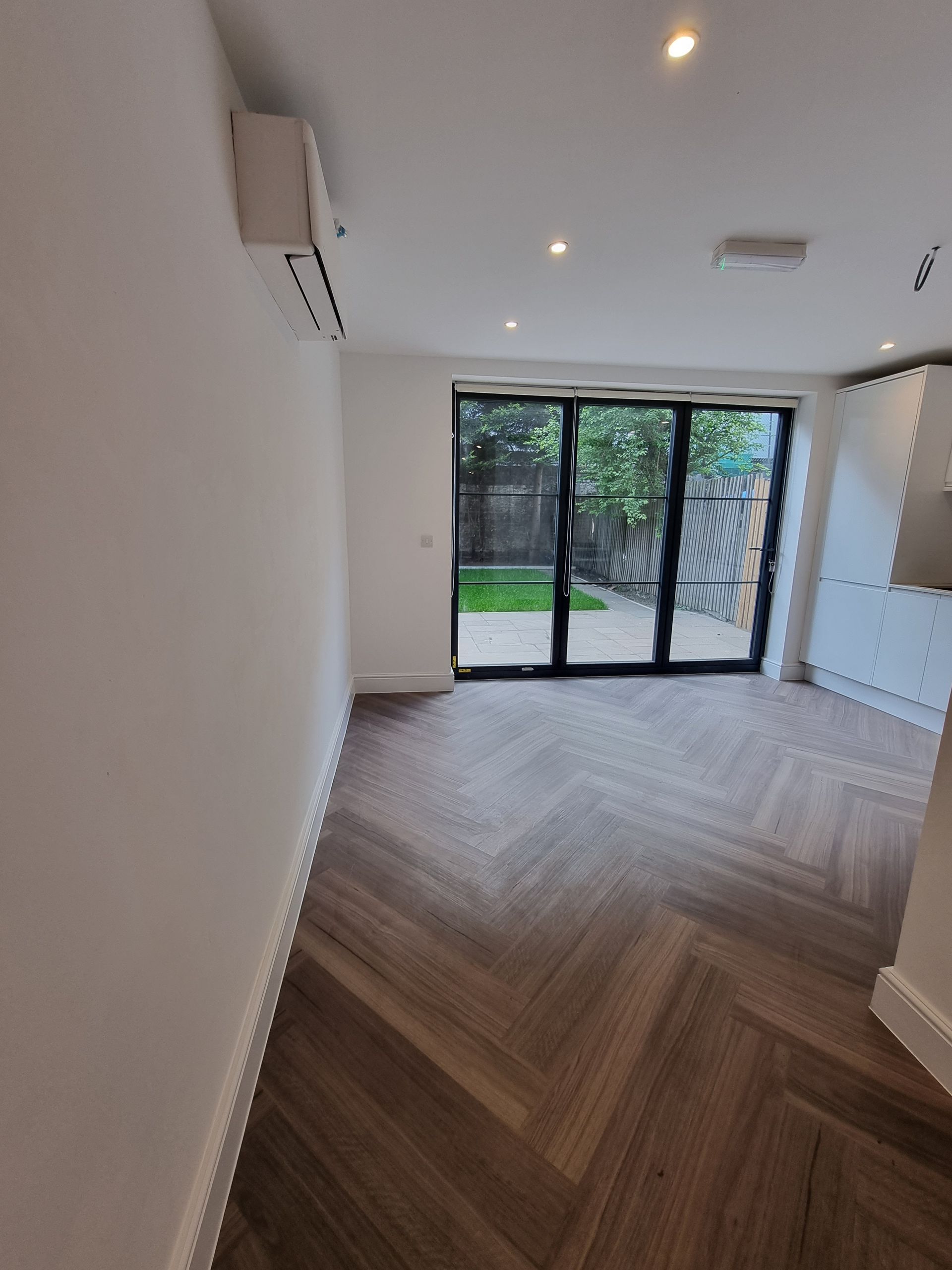 Interior room with herringbone wood floor, sliding glass doors to yard. Air conditioning unit on wall.