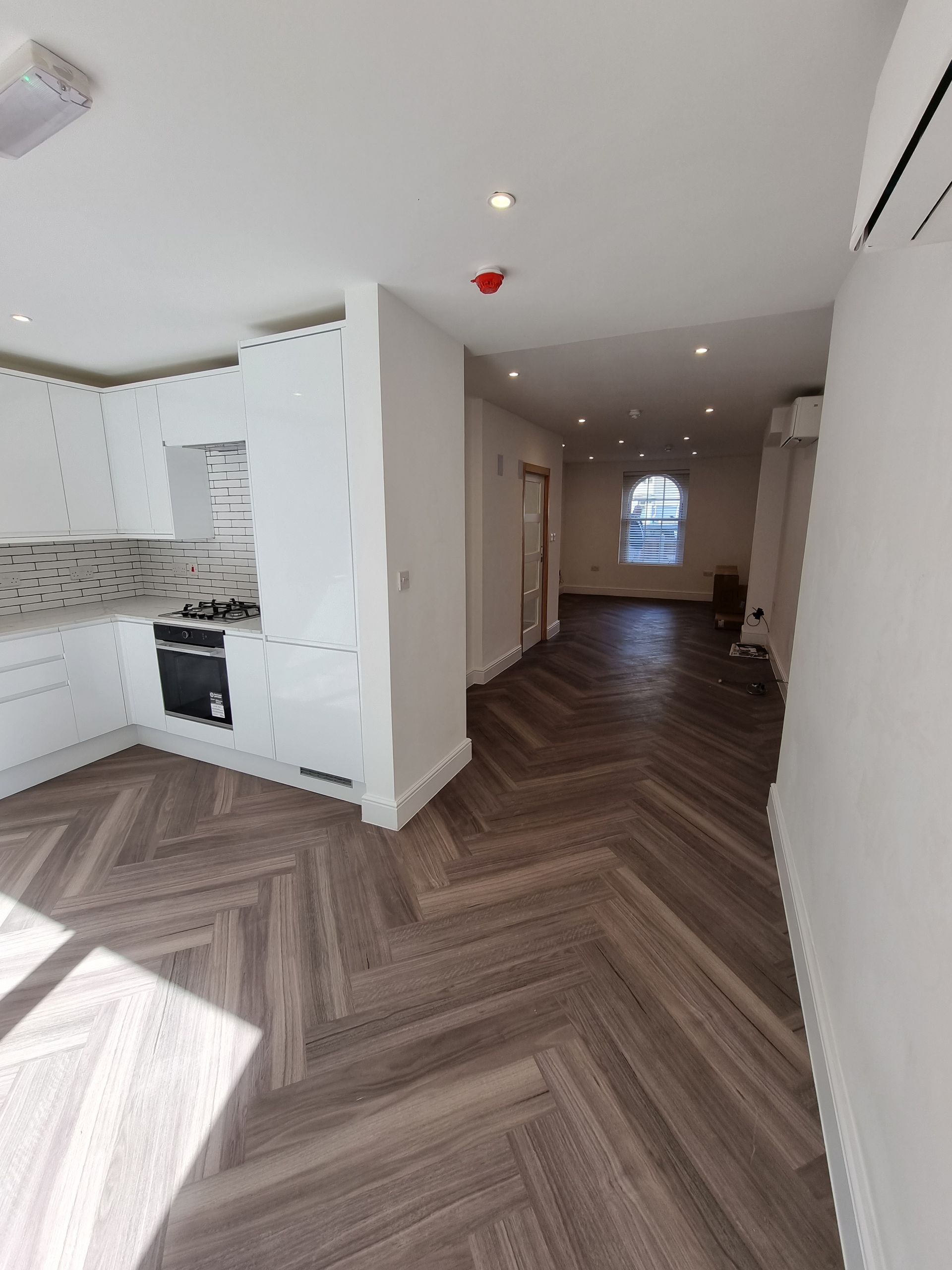 Interior view of a modern kitchen with white cabinets, dark wood flooring, and a hallway.