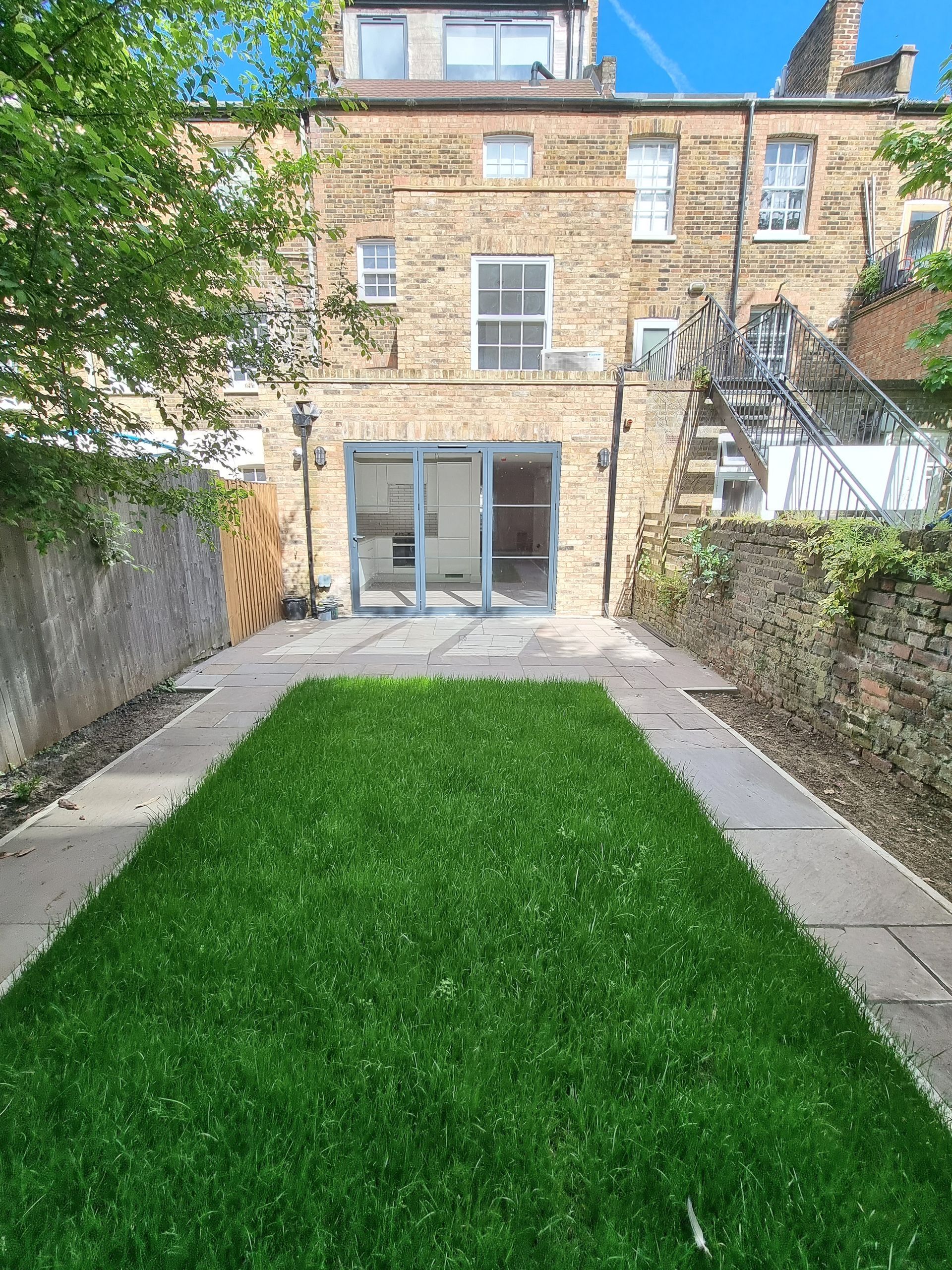 Backyard with green grass, stone patio, and building with glass doors and windows.
