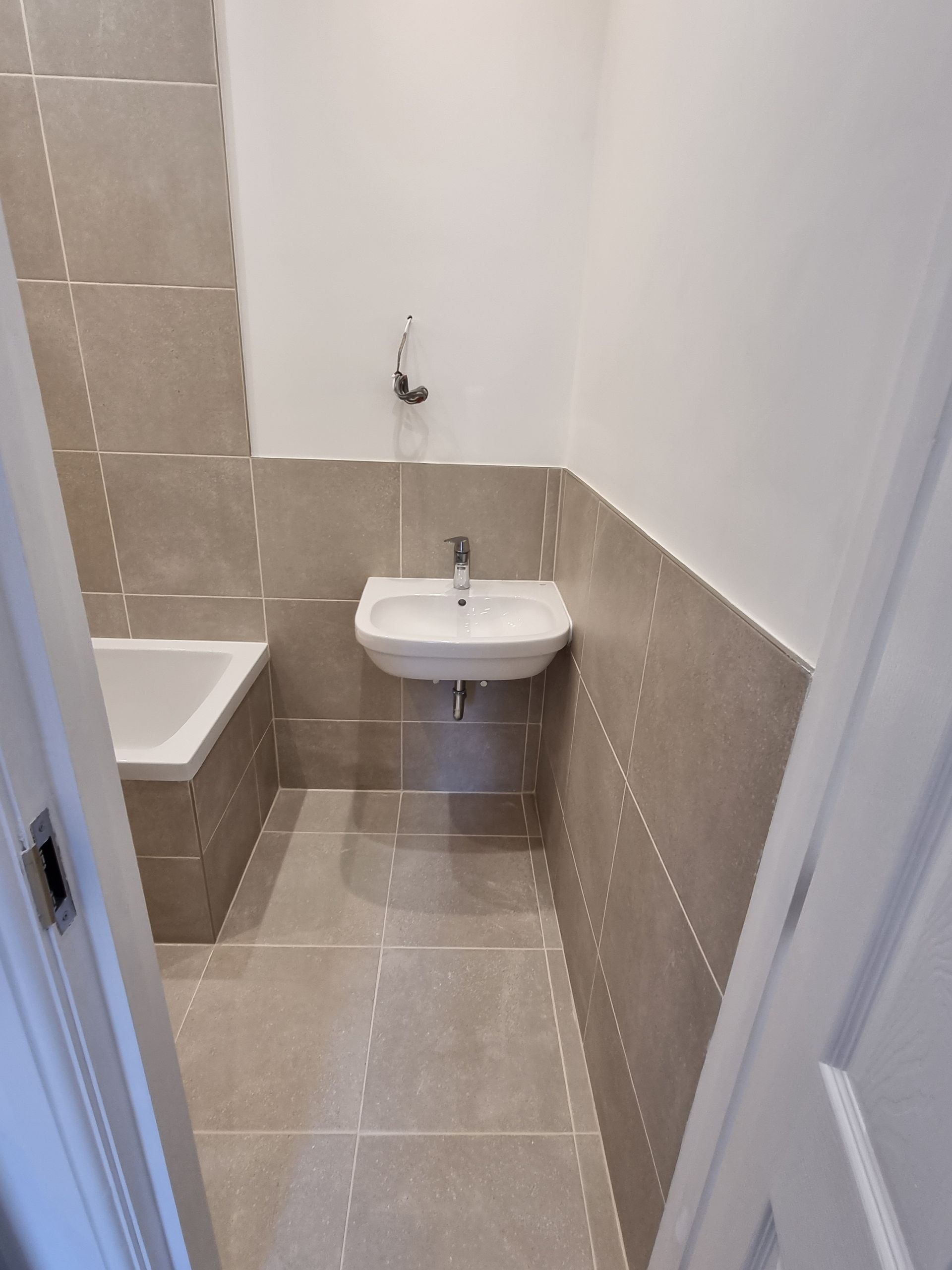 Small bathroom with a tub, sink, and neutral-colored tiled walls and floor.