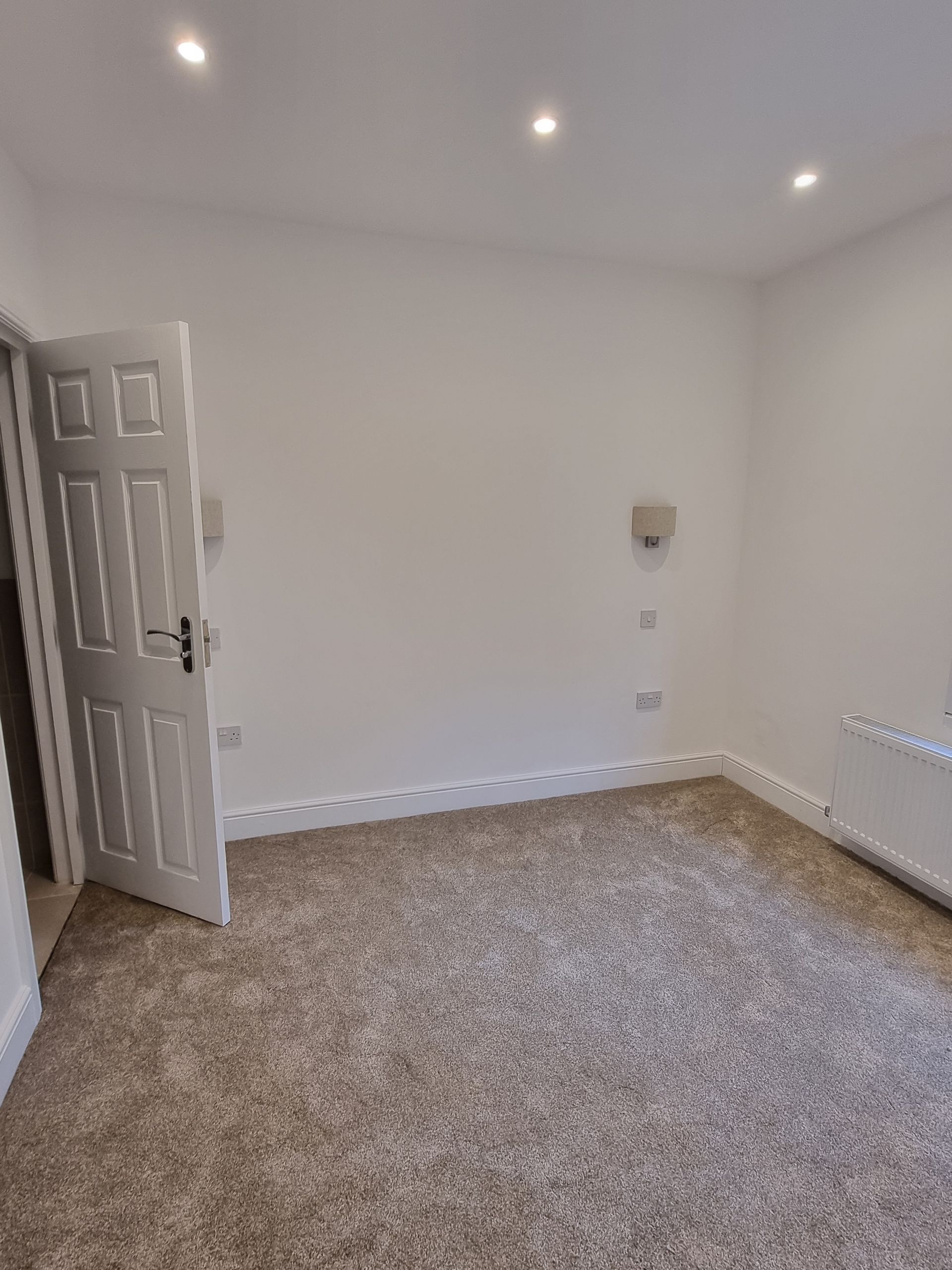 Empty room with carpet, white walls, open door, and recessed lighting.