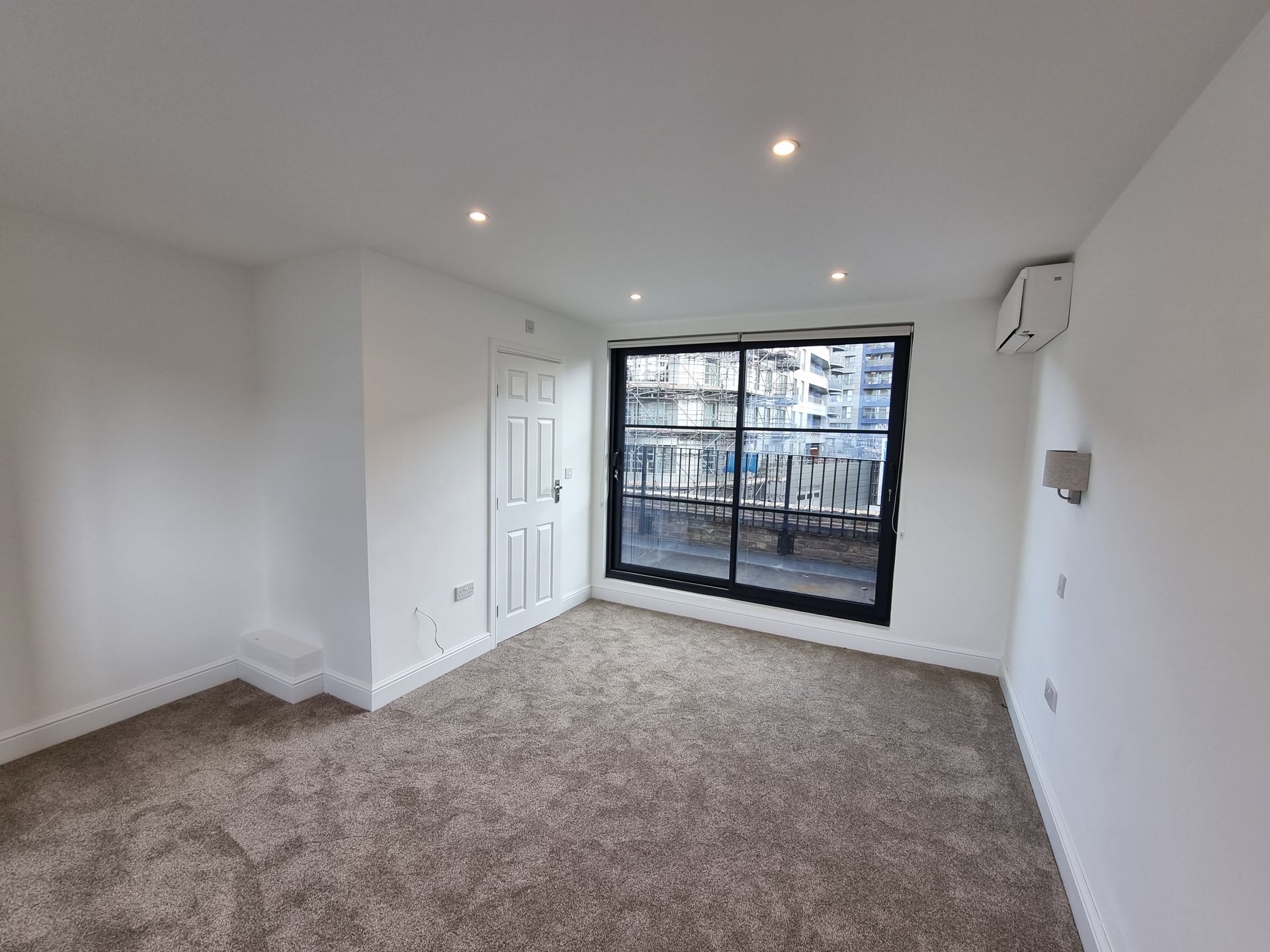 Empty room with brown carpet, white walls, closet, and a window with a balcony.