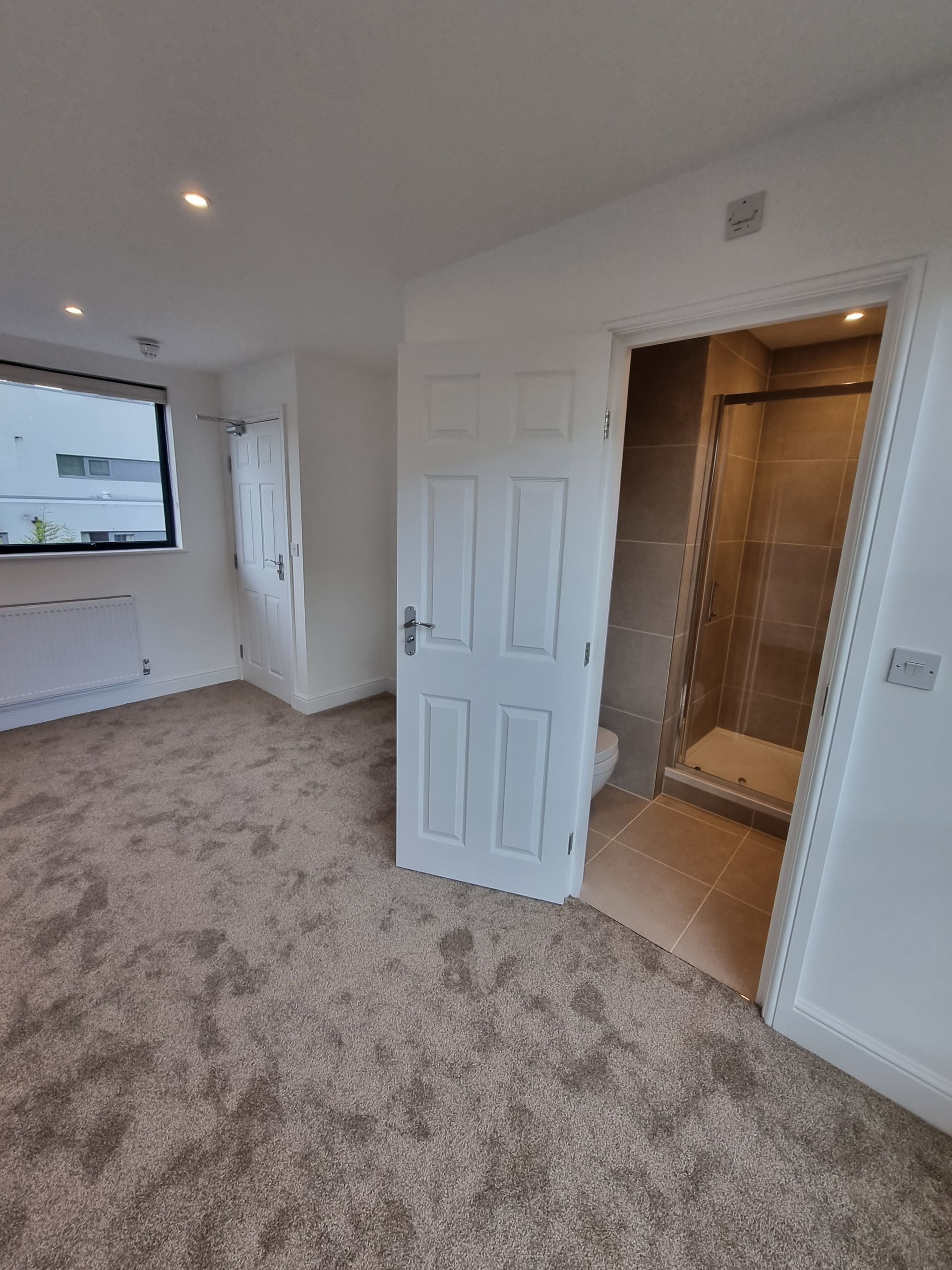 Bedroom with gray carpet, white walls, and a door open to a bathroom with a shower.