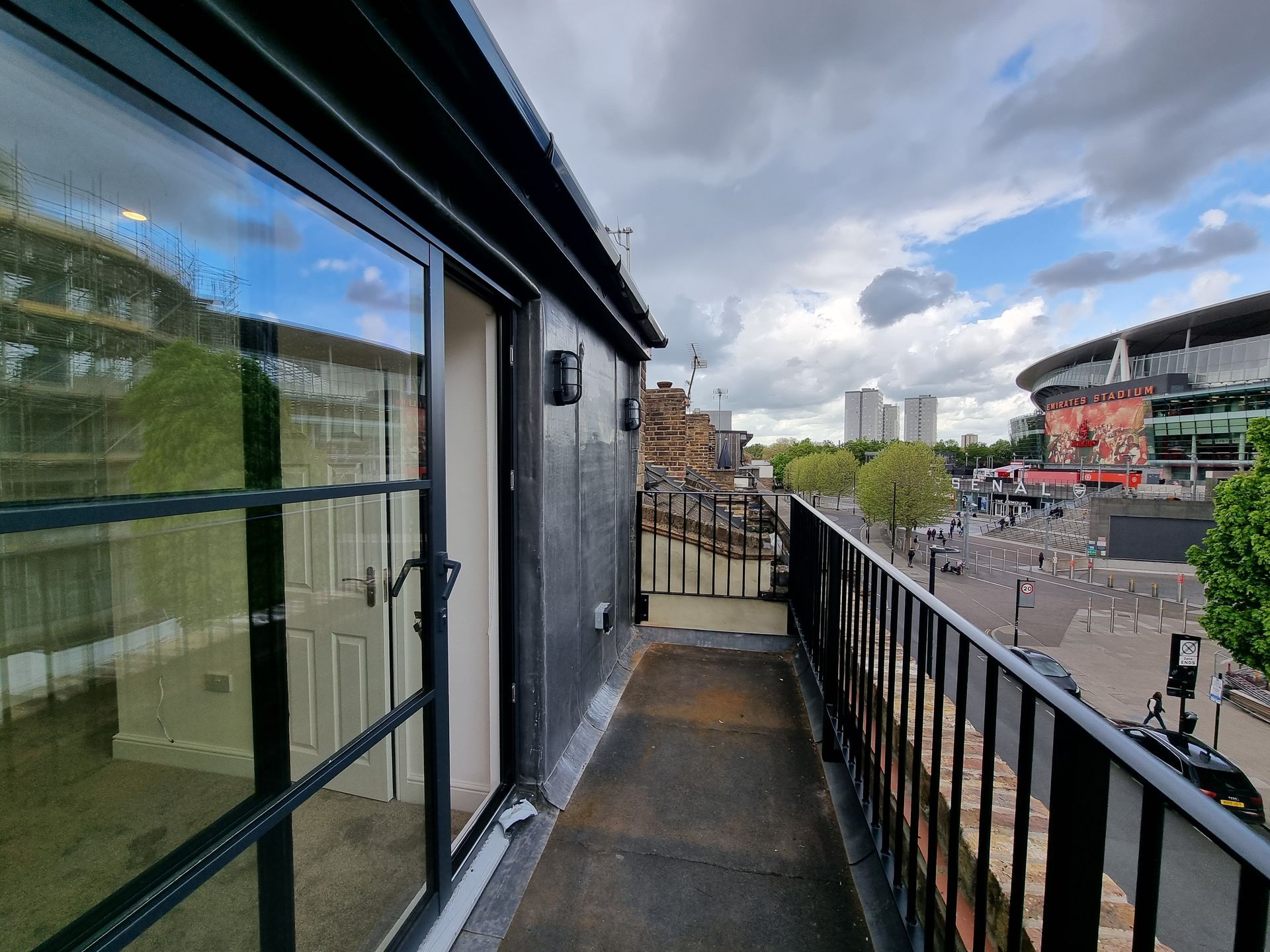 Balcony overlooking a street with a stadium in the background, cloudy sky.