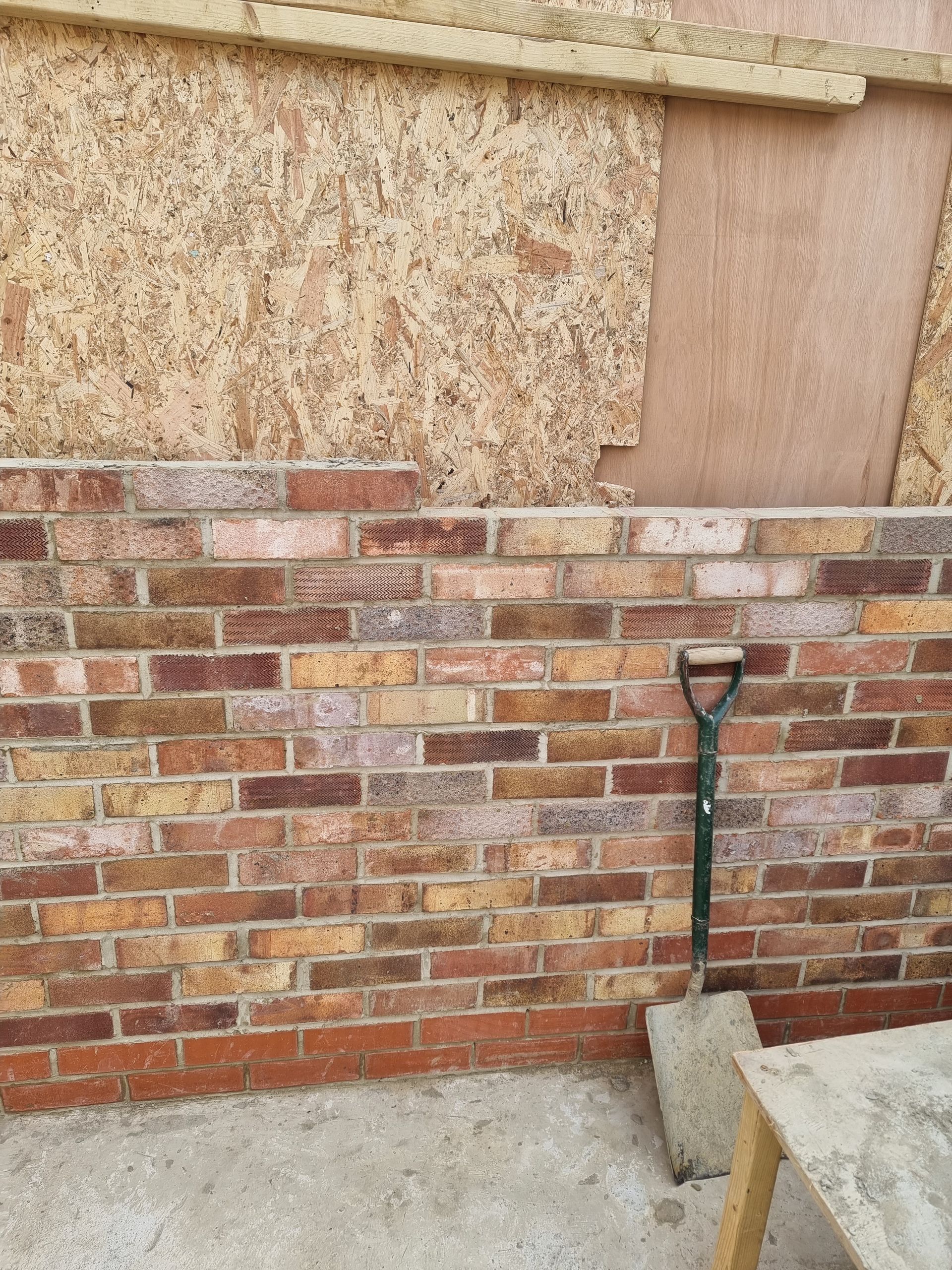 Brick wall with a shovel leaning against it, and wooden wall panels above.