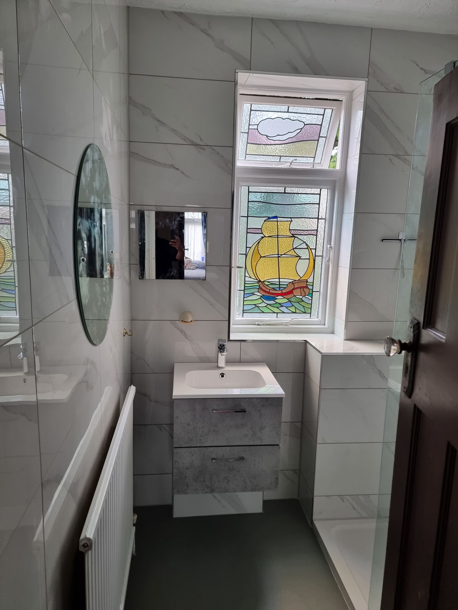 Bathroom with white marble-look tile, vessel sink, stained glass window depicting a ship, and a radiator.