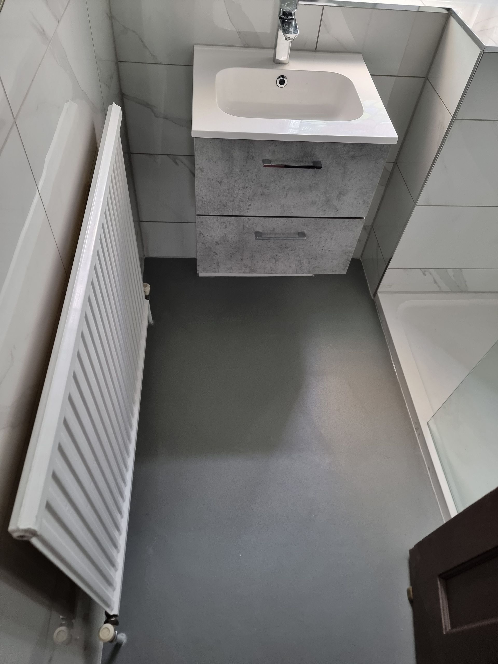 Bathroom with gray flooring, a white sink with two drawers, and a radiator.