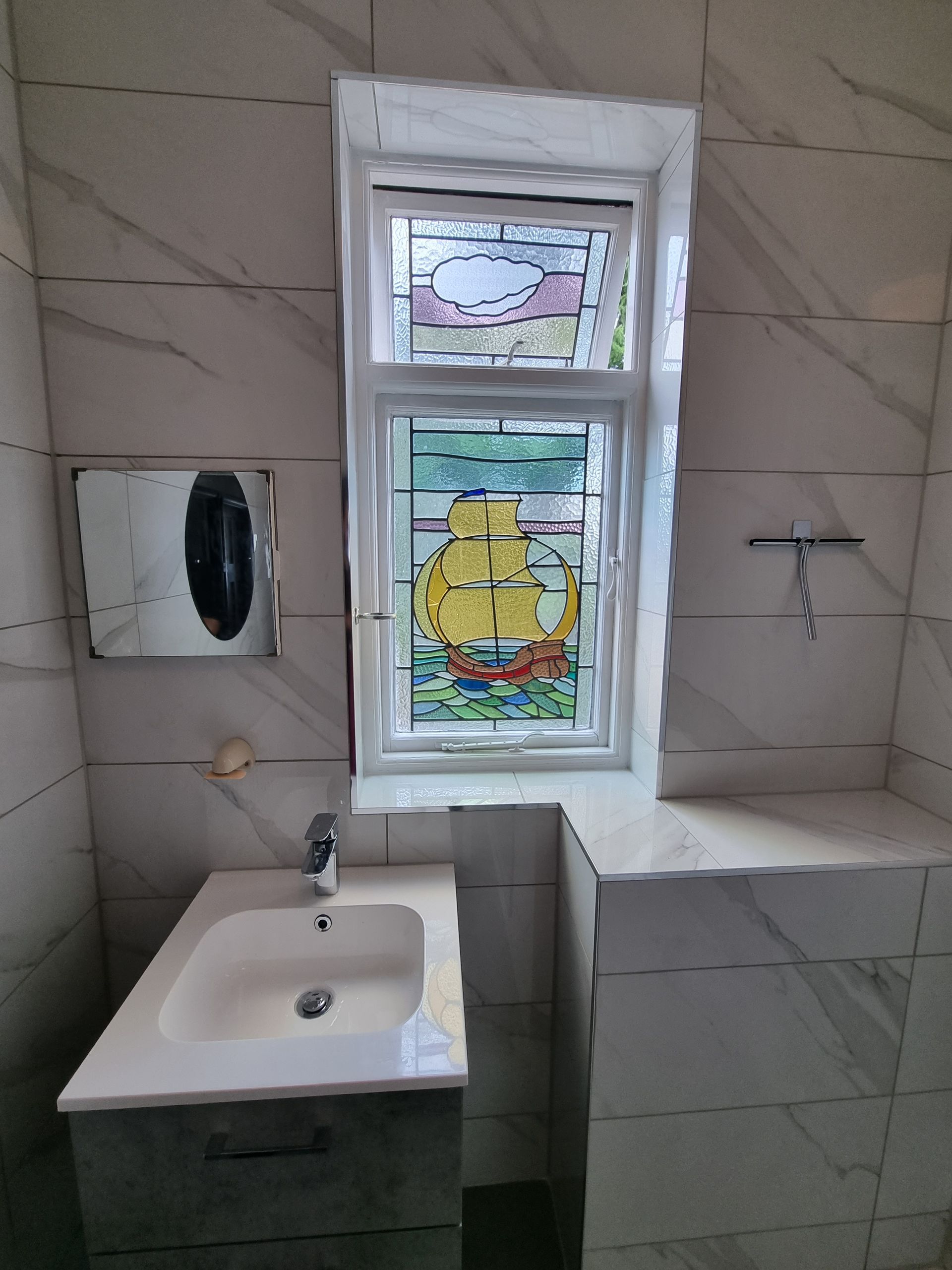 Bathroom with stained glass window, sink, and tiled walls. The window features a ship design.