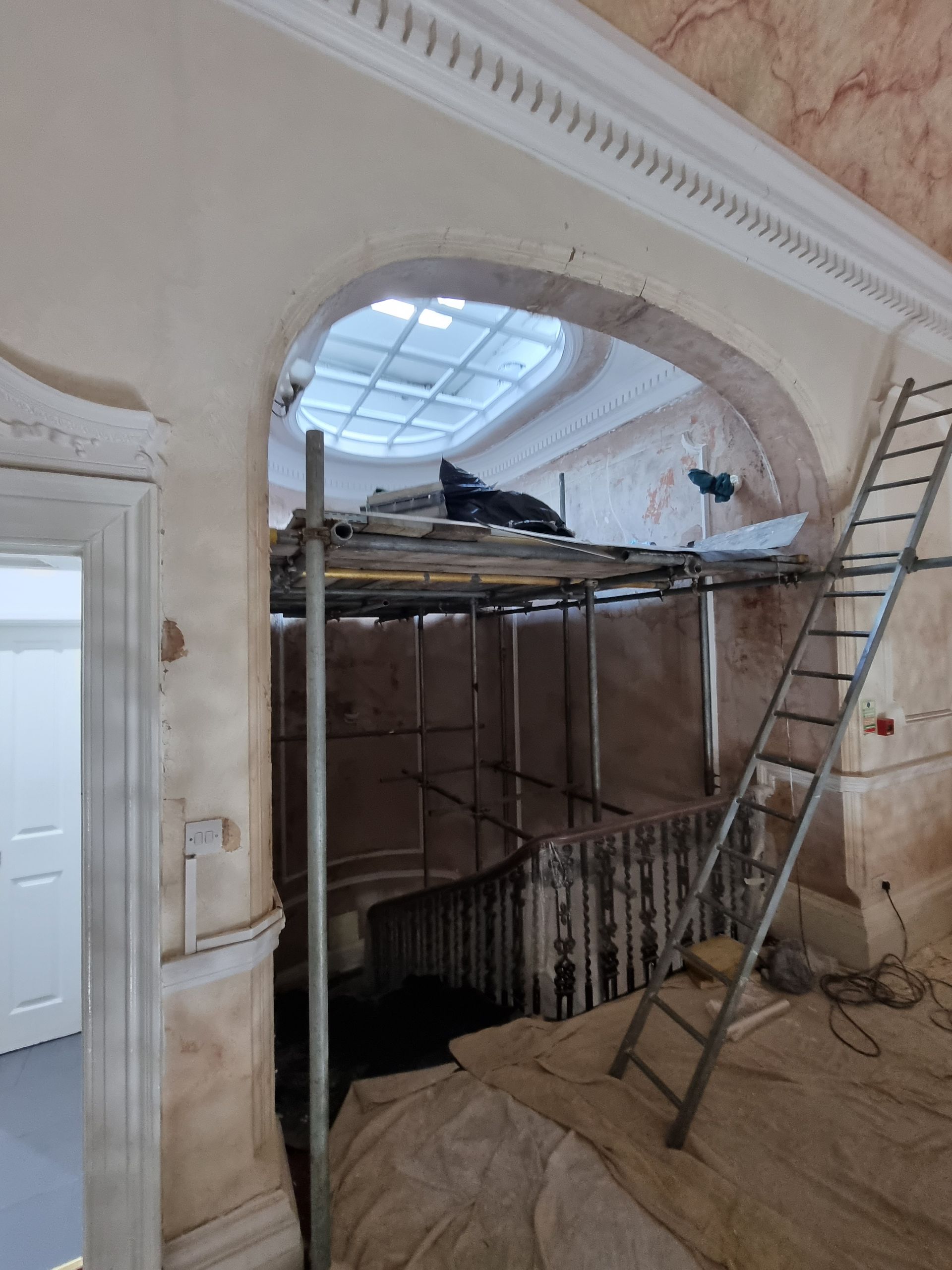 Interior staircase under renovation; scaffolding, ladder, arched opening.