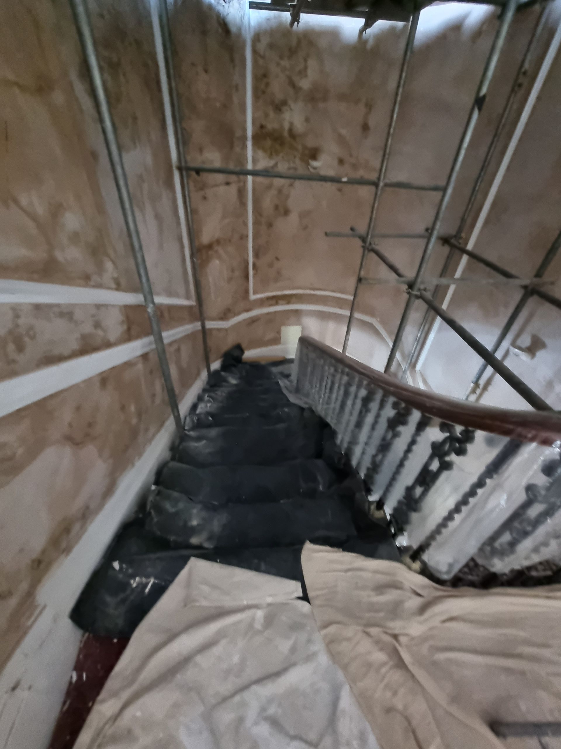Stairwell under renovation: scaffolding, covered stairs, and damaged walls.