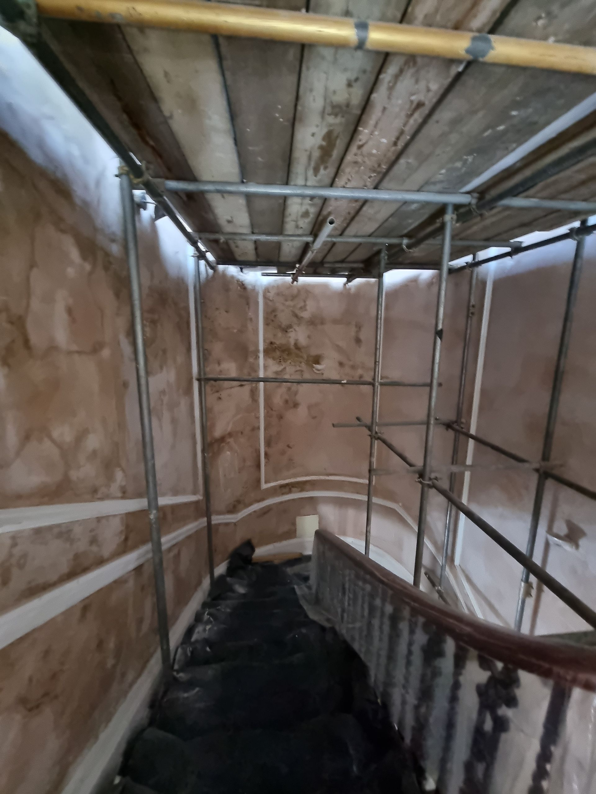 Scaffolding covers a curved staircase with damaged walls.