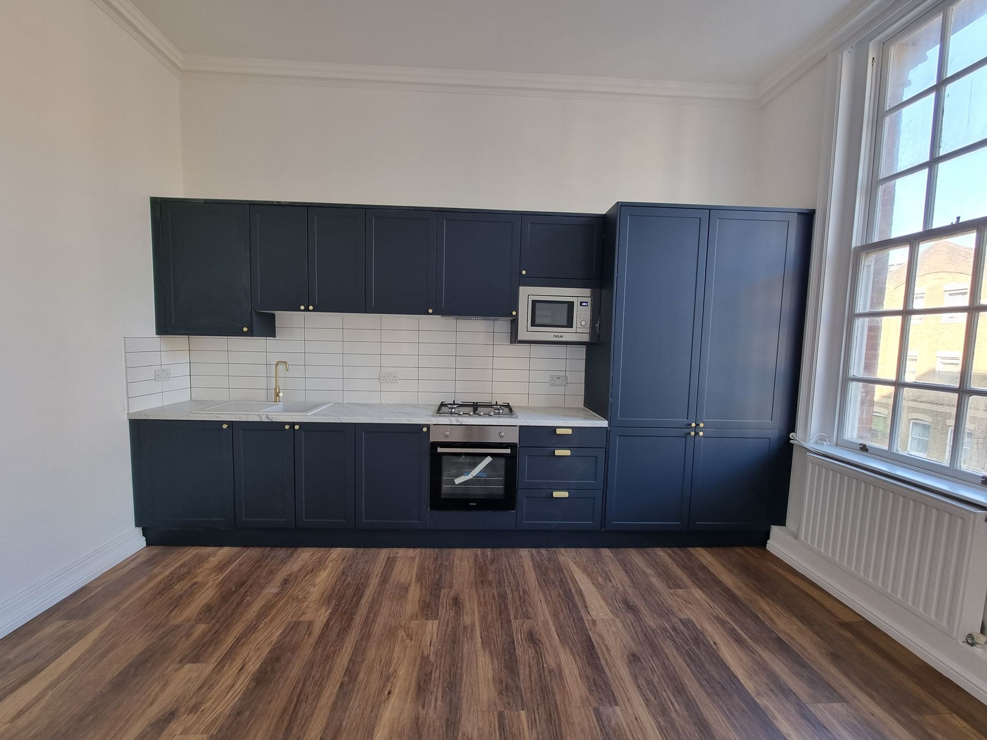 A kitchen with blue cabinets , a stove , a microwave and a window.