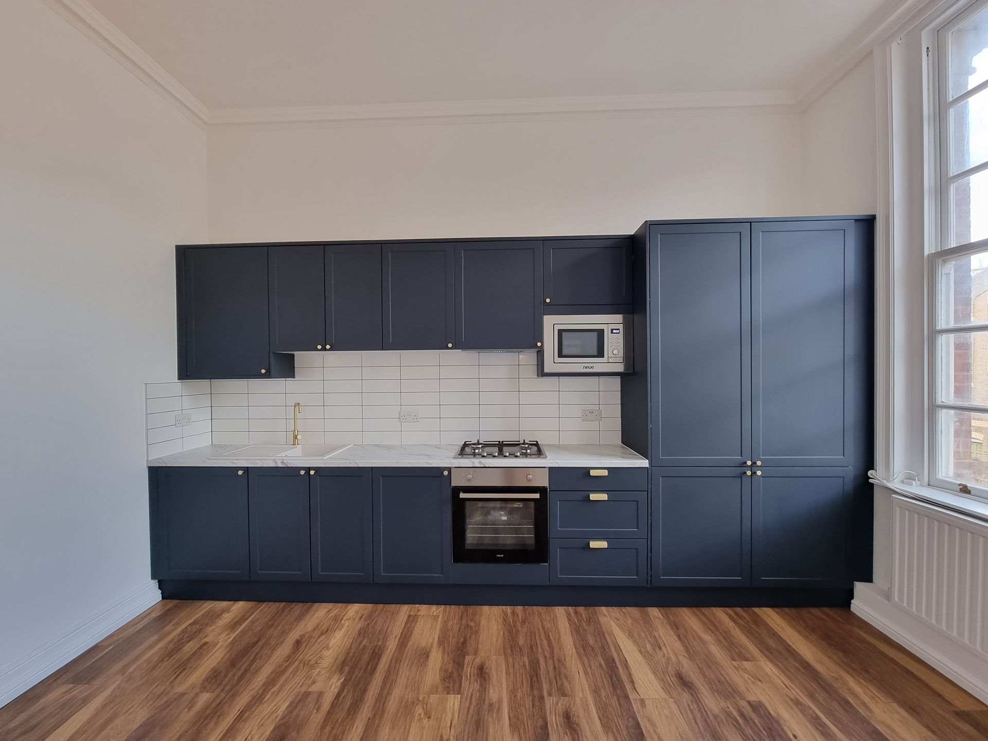 An empty kitchen with blue cabinets and hardwood floors