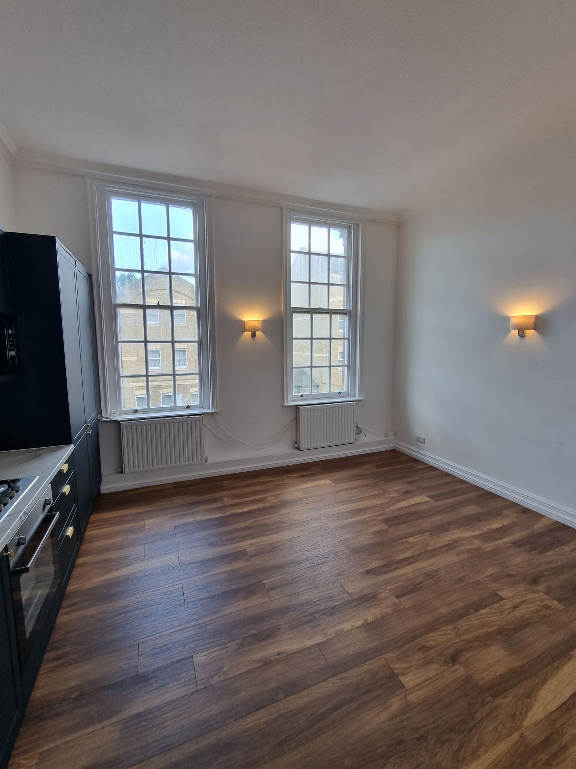 An empty room with hardwood floors and two windows.