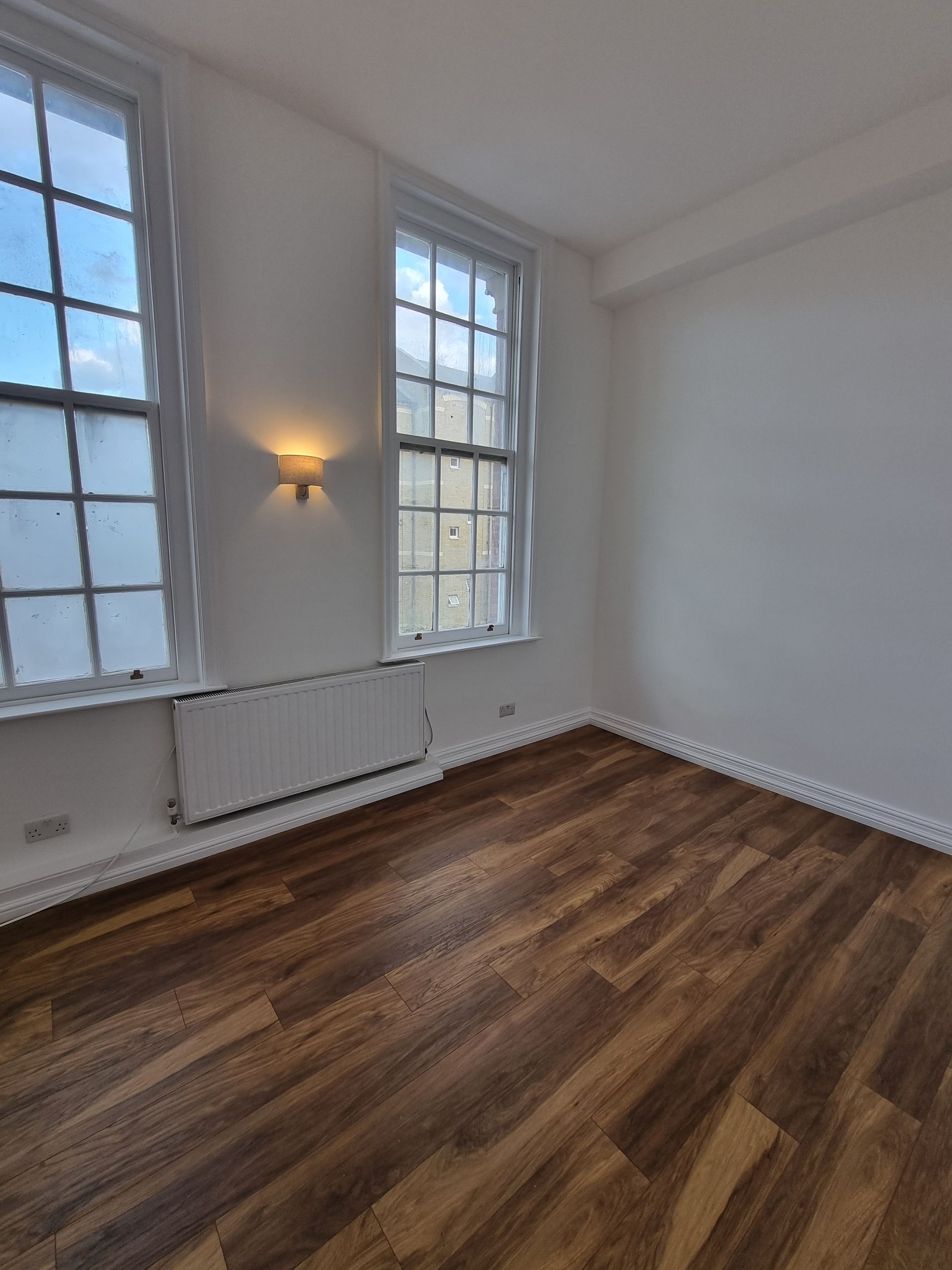 An empty room with hardwood floors and two windows